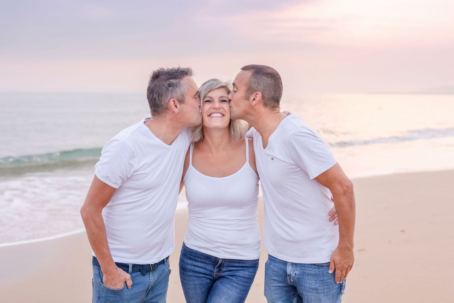 Sweet moment captured on beach with three people in matching outfits at sunset.