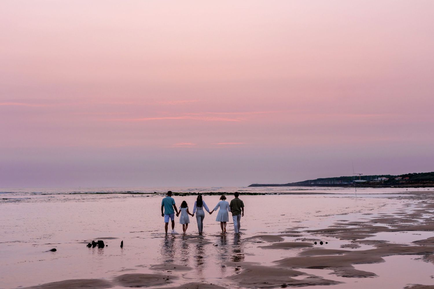 Silhouettes of people holding hands while walking on beach at dusk.
