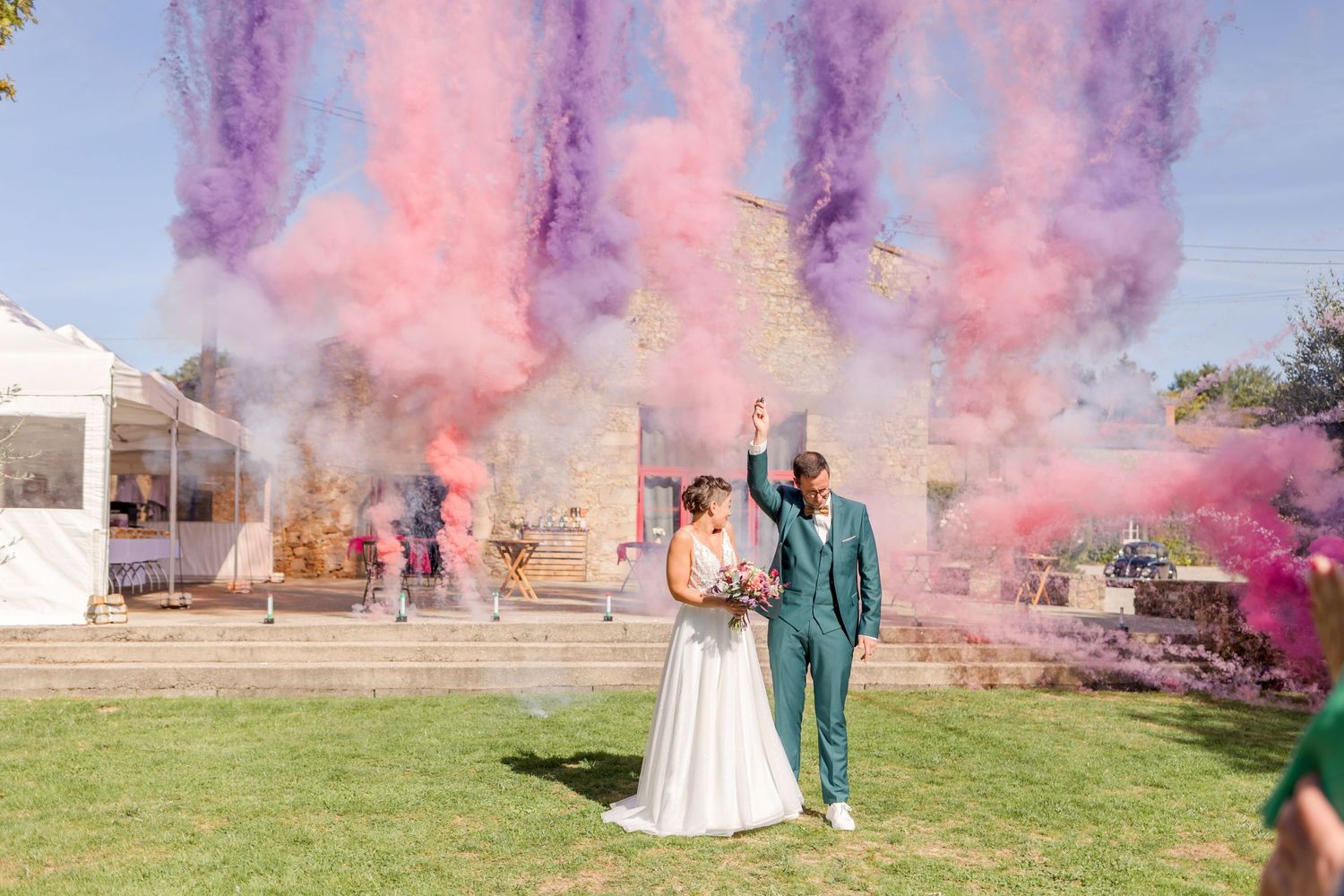 Pink and purple smoke bombs create a dramatic effect at an outdoor celebration.