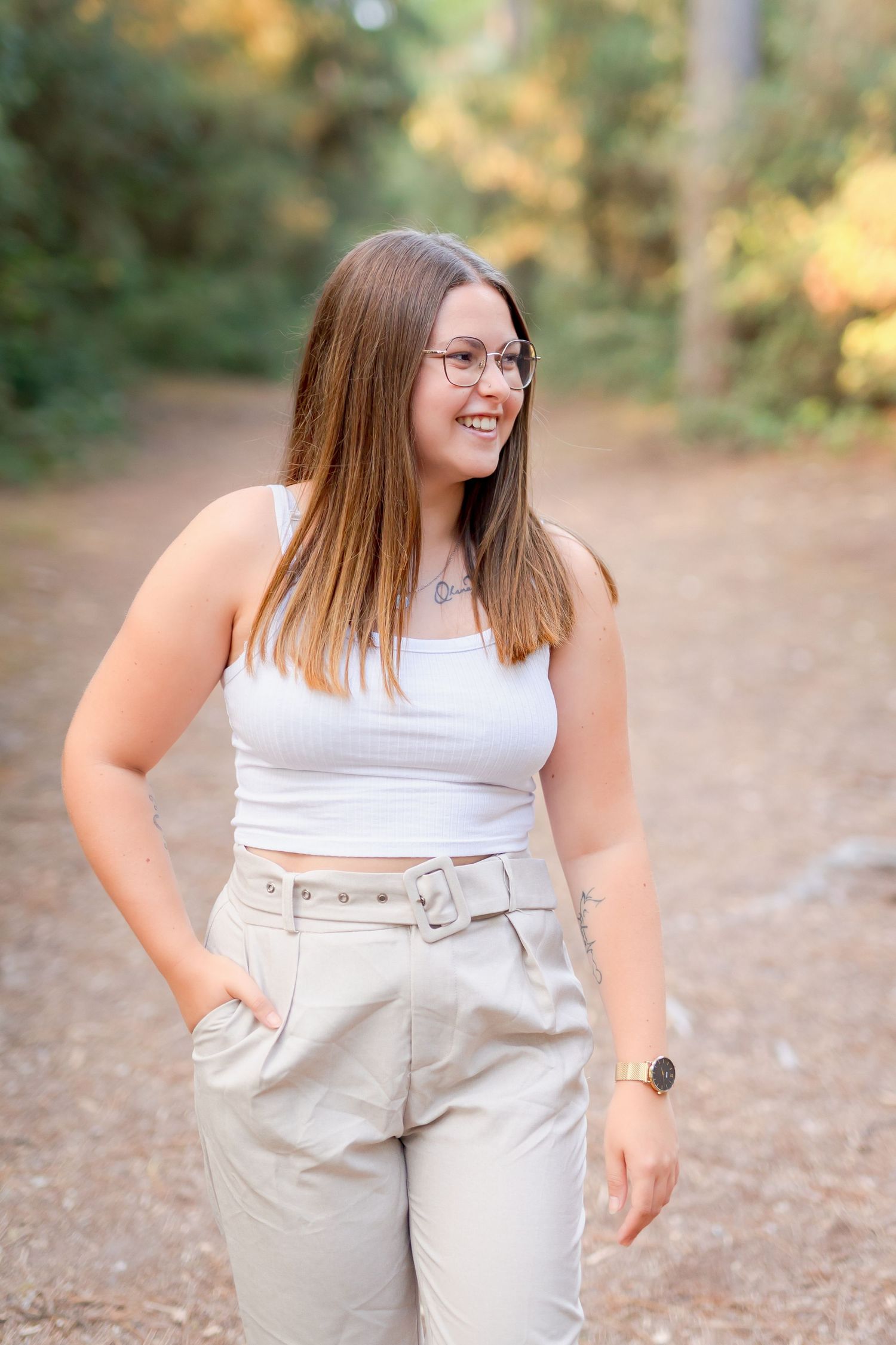 A casually dressed person in a white top and beige pants poses on a forest path.