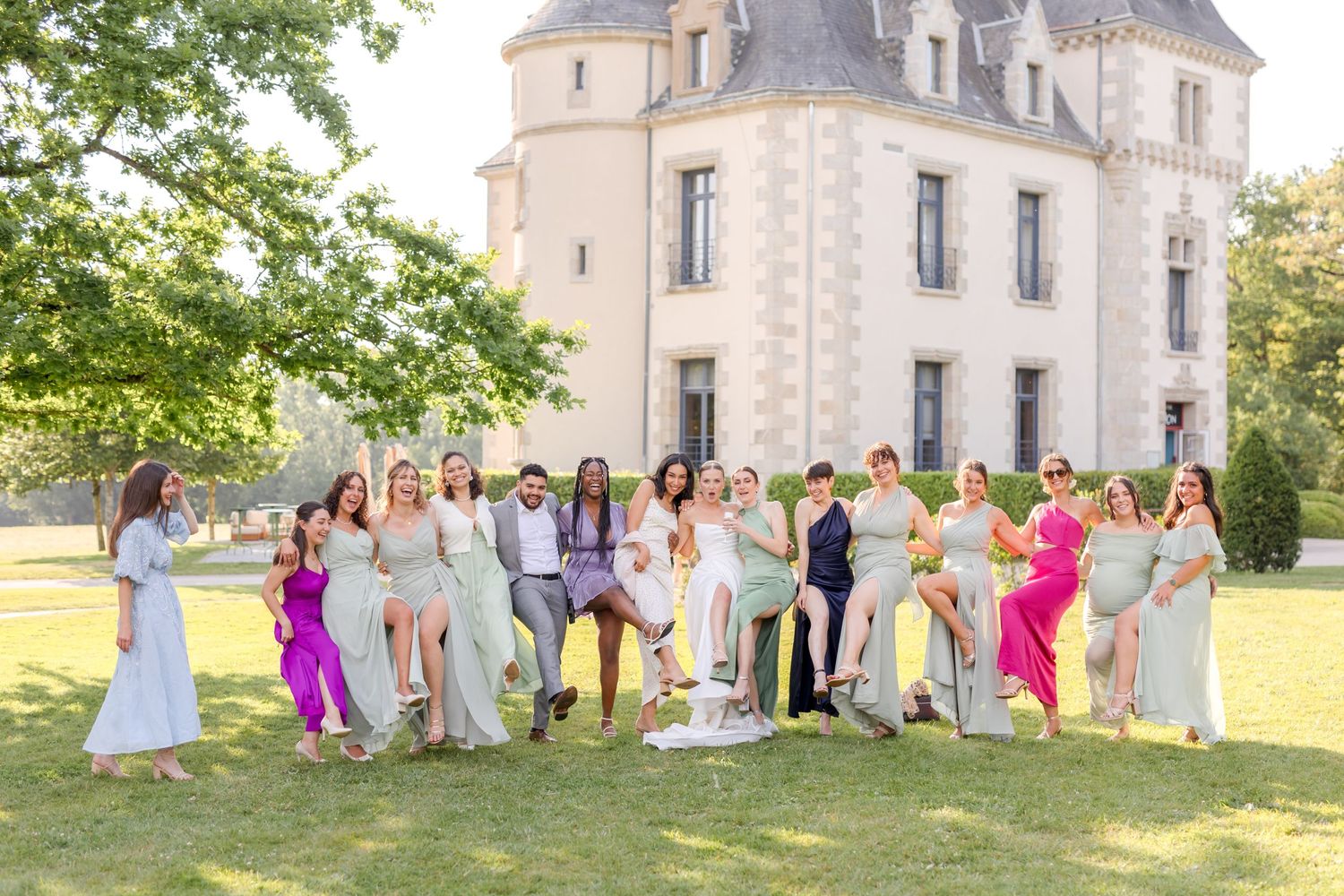 Group photo of wedding guests in colorful dresses gathered outside a French chateau.