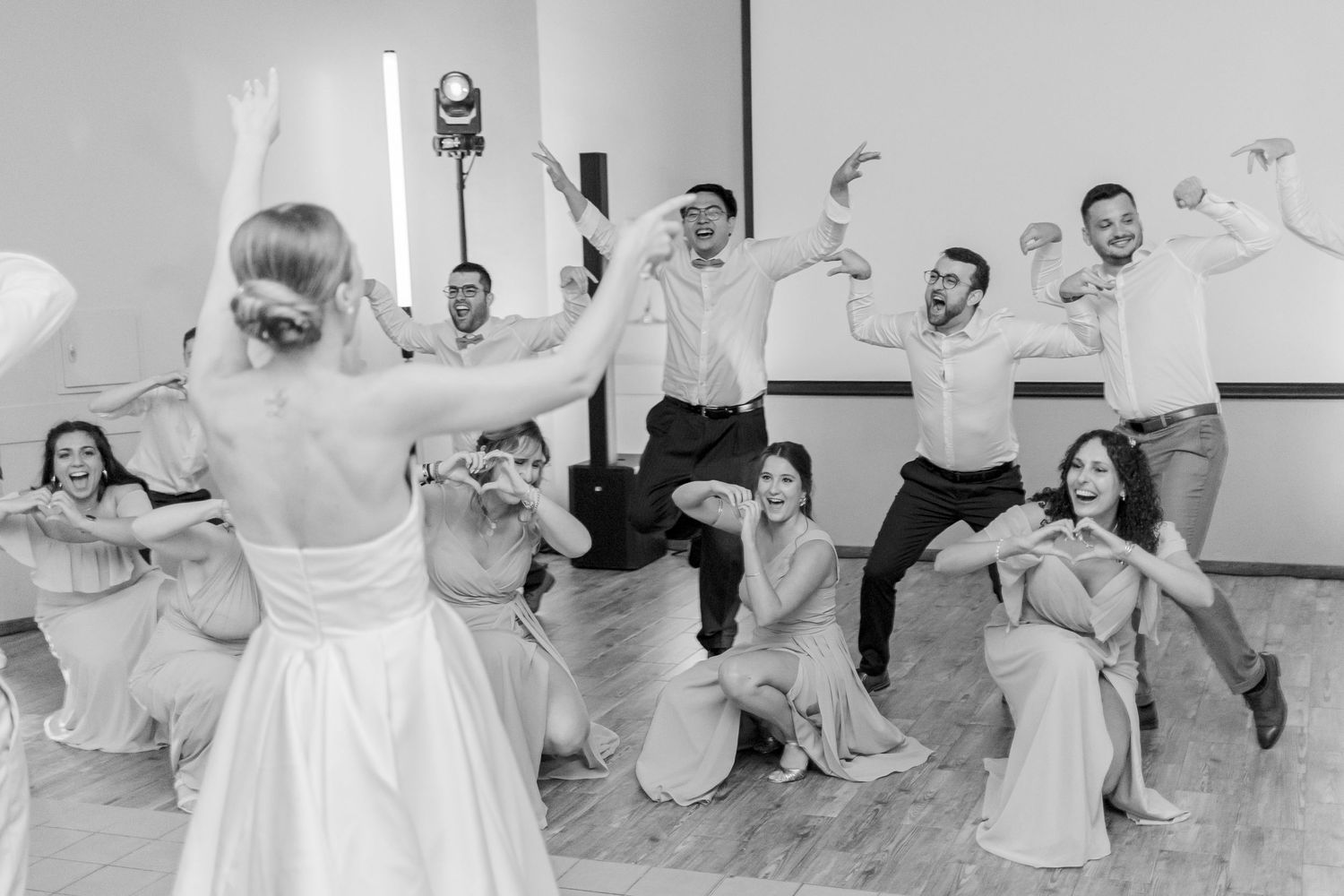 Wedding party members dance and pose energetically in black and white photo.