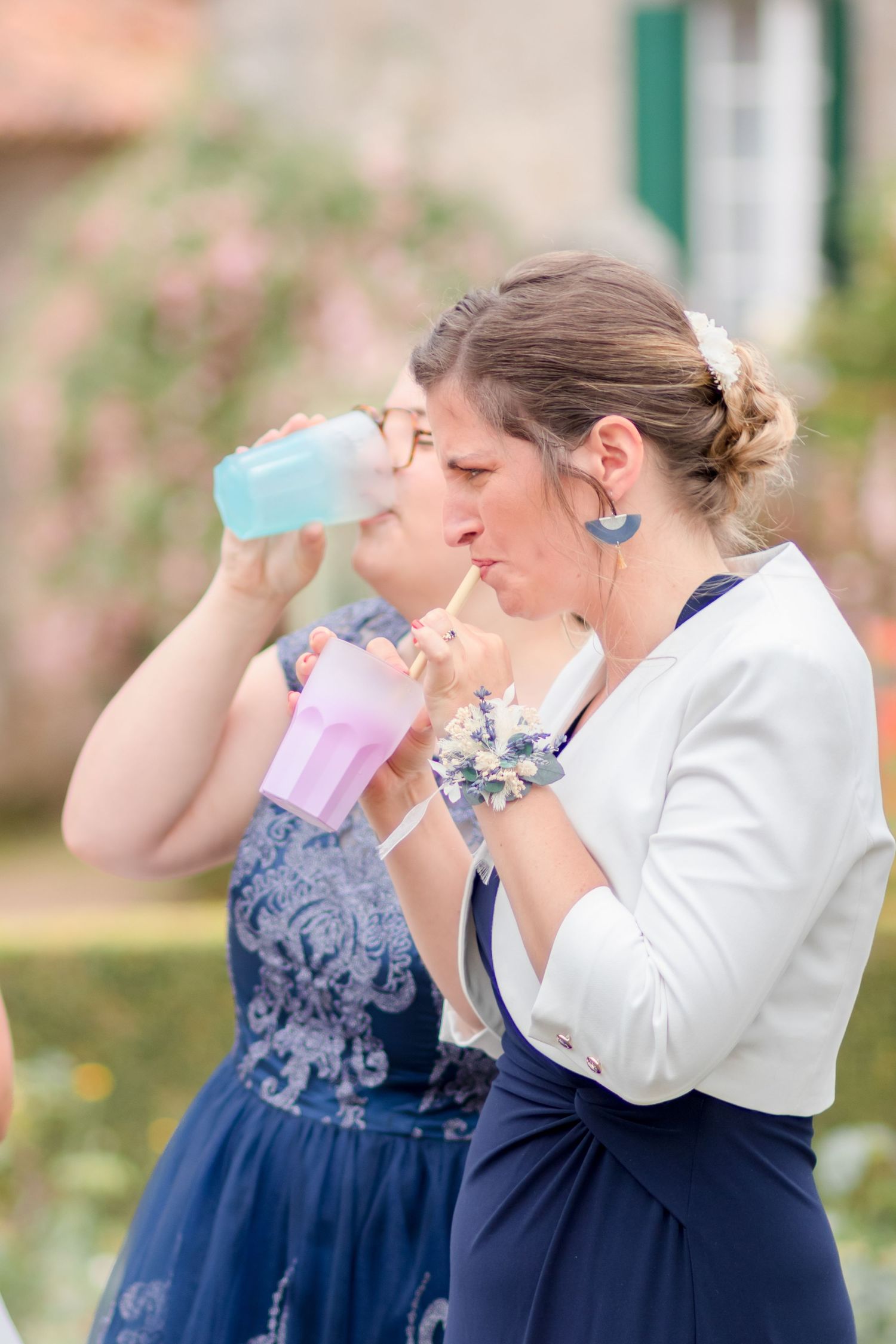 Wedding party members in navy blue dresses and white outfits sipping drinks together at an outdoor celebration.