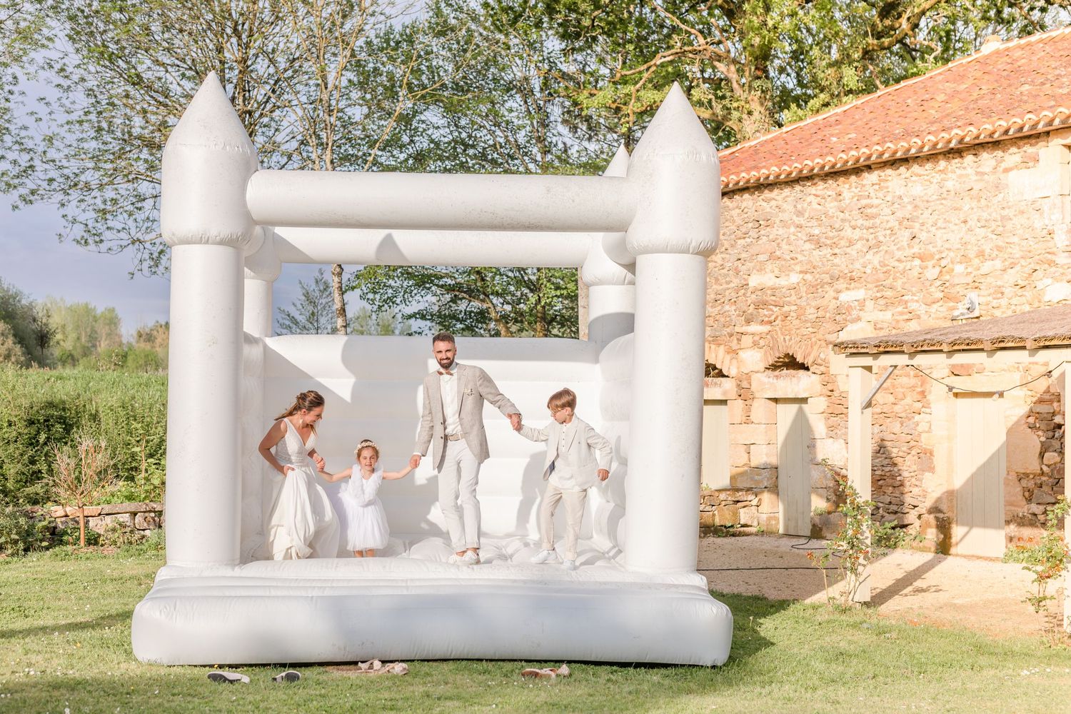 White inflatable bounce house at outdoor wedding venue with stone wall backdrop.