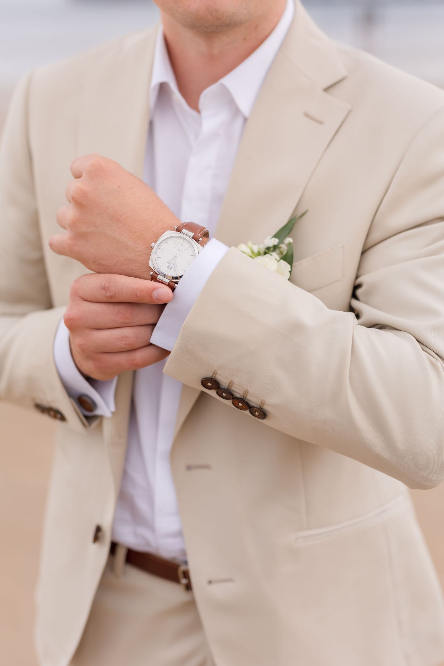Close-up of groom adjusting his watch while wearing a beige suit and white dress shirt.