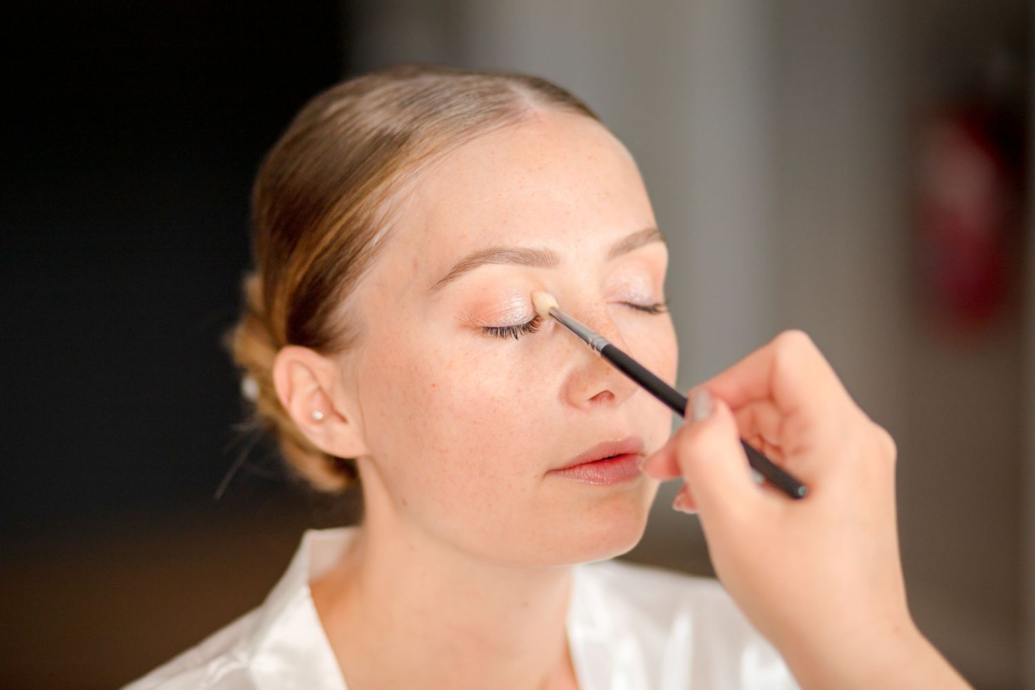 Professional makeup artist applies eye makeup to client during bridal beauty preparation.