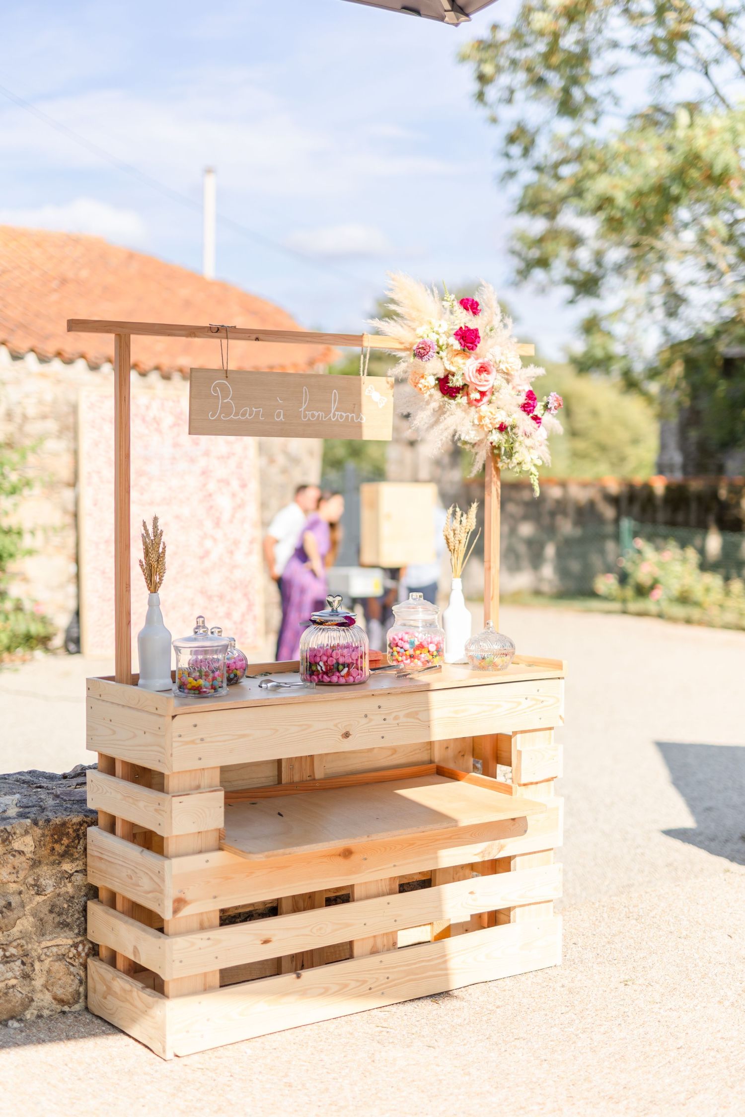 Rustic wooden pallet display stand decorated with pink and red flowers at an outdoor event.