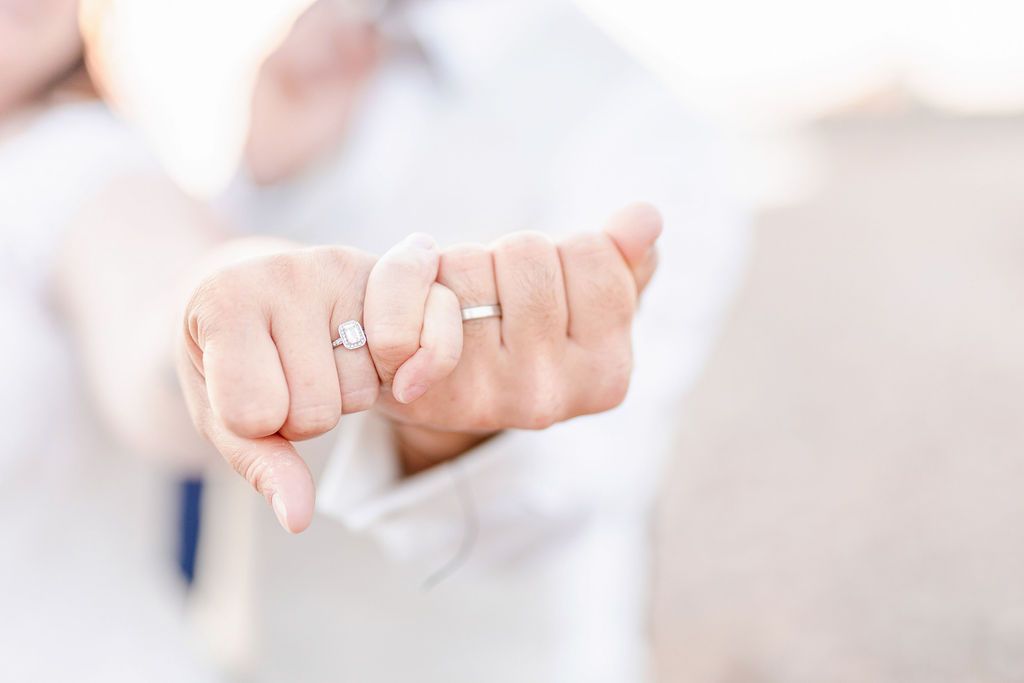 Close-up of wedding rings displayed on intertwined hands against a bright background.