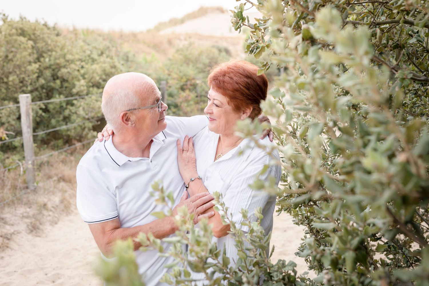 Candid outdoor family photo session showing multiple generations in coordinated white outfits against a natural backdrop.
