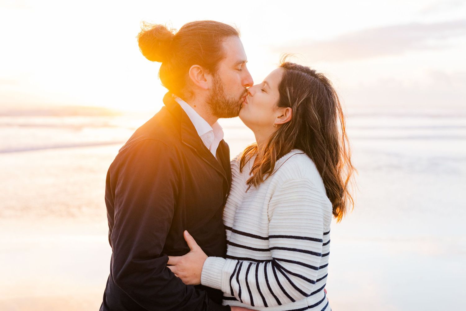 Golden hour maternity photos capturing couple's tender moments on beach.