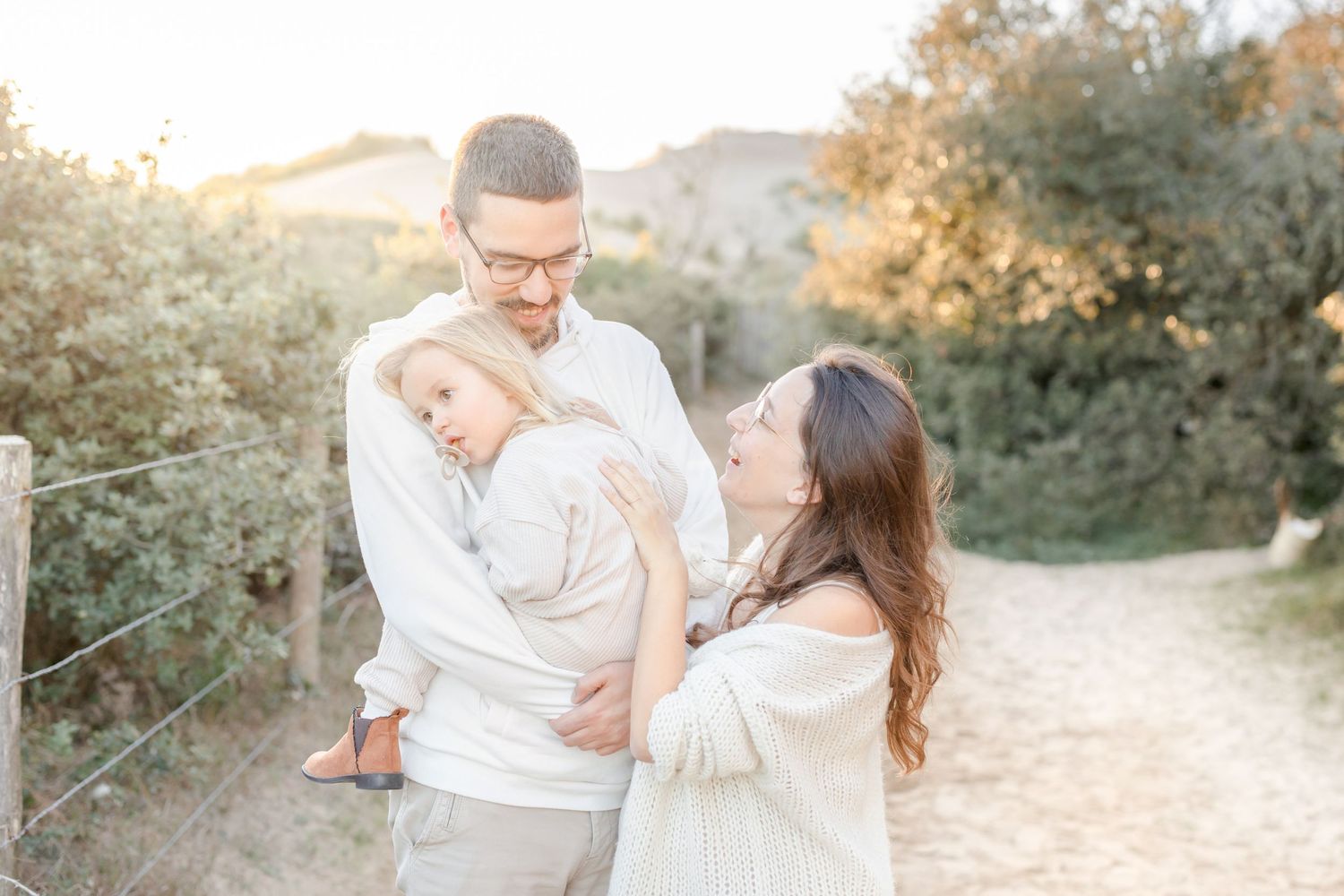 Family in white outfits share tender moment together during golden hour photoshoot outdoors.