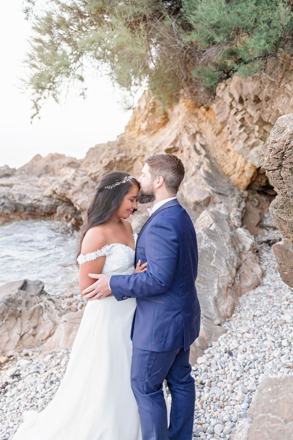 Romantic moment between newlyweds against dramatic rocky coastal backdrop.