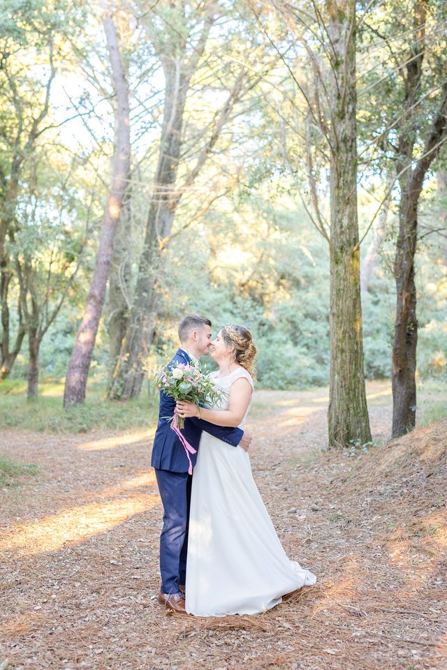 A couple dancing in a sunlit forest setting with fallen leaves and dappled light.