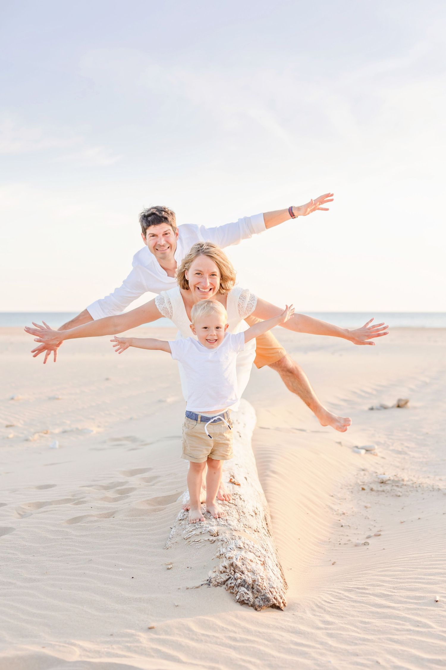 Family members spread their arms while balancing on a sand ridge at the beach during sunset.