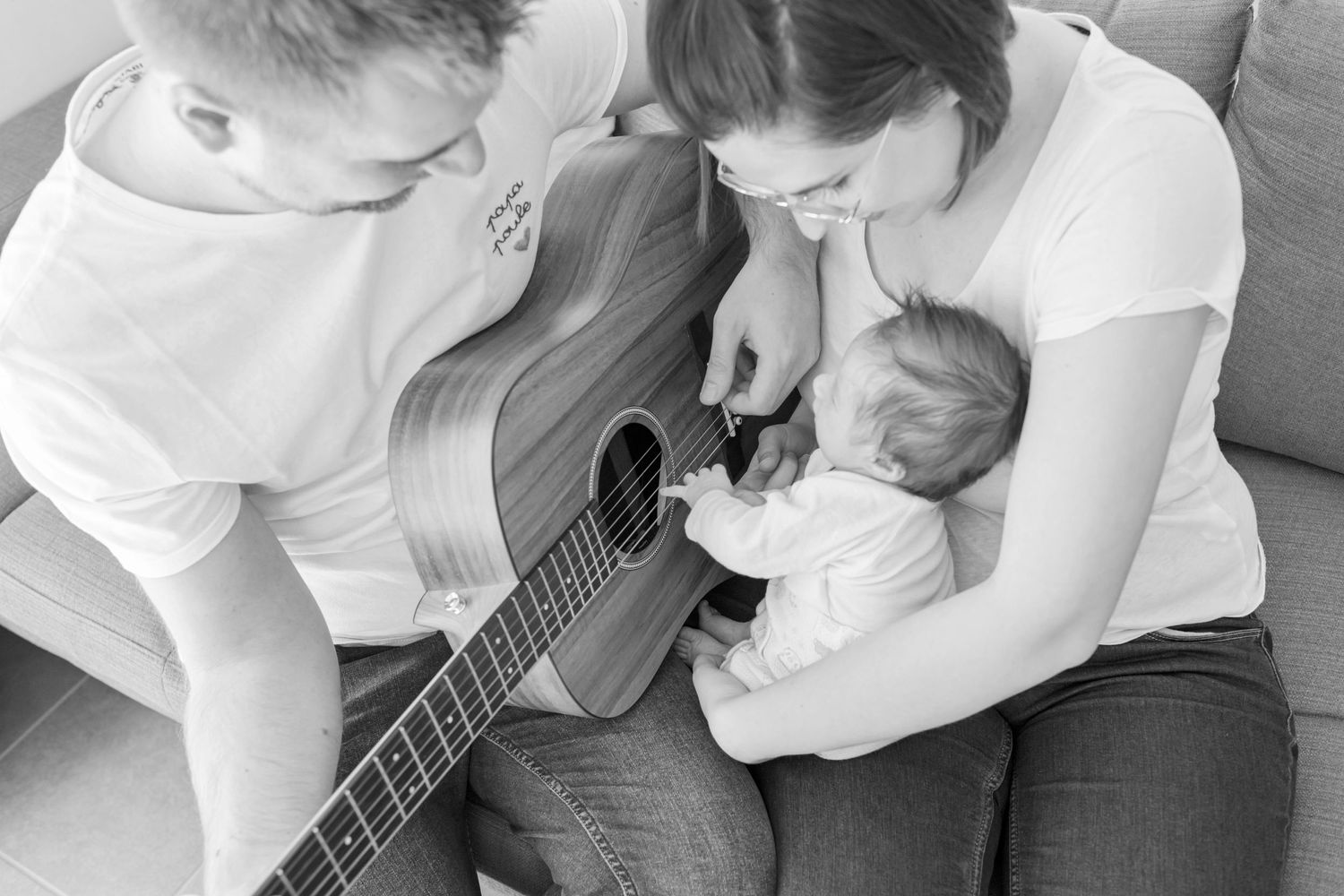 Black and white photo of a tender family moment on a couch with a small musical instrument.