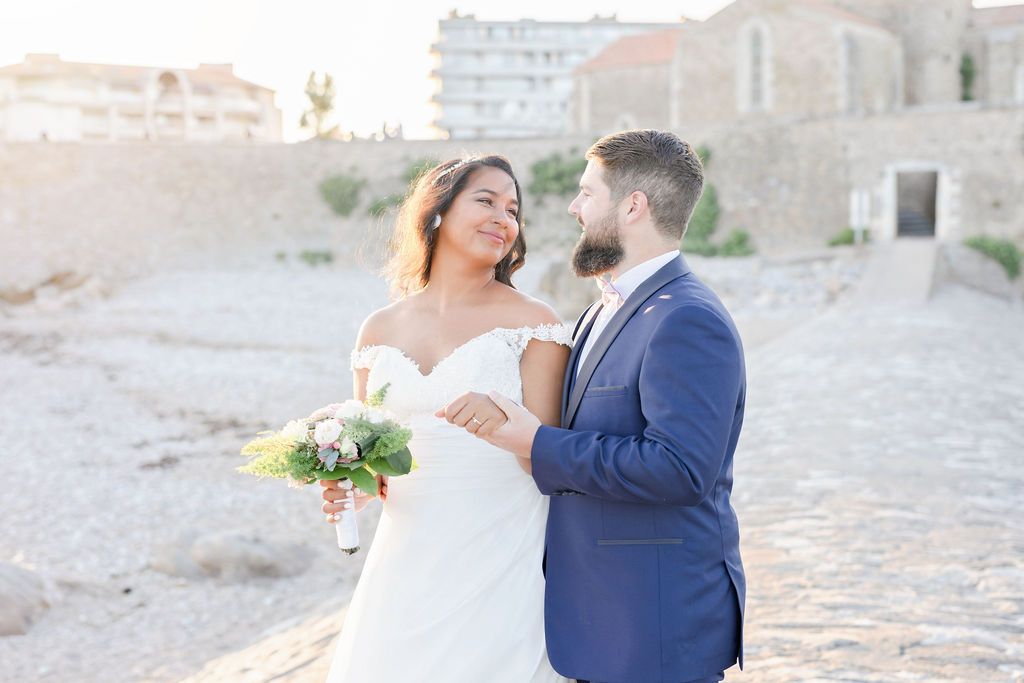 Wedding couple shares intimate moment on sunlit cobblestone path by stone building.