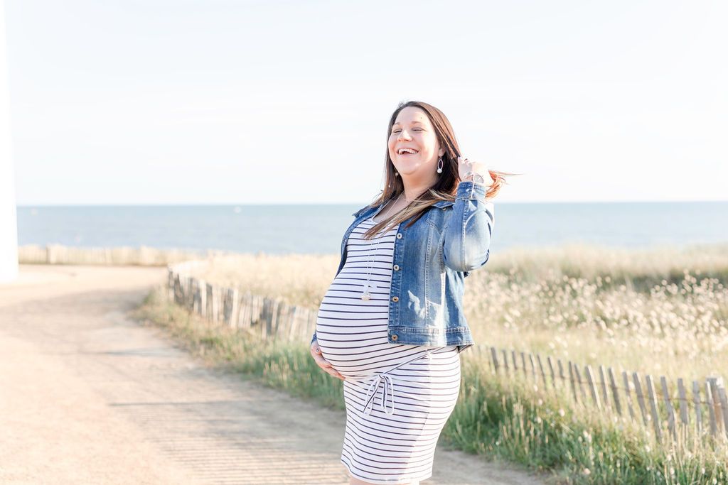 Happy expecting person in casual attire enjoying a sunny day by the sea.