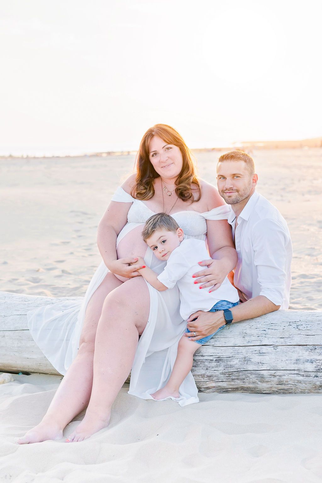 Family relaxes together on driftwood at beach during golden hour.