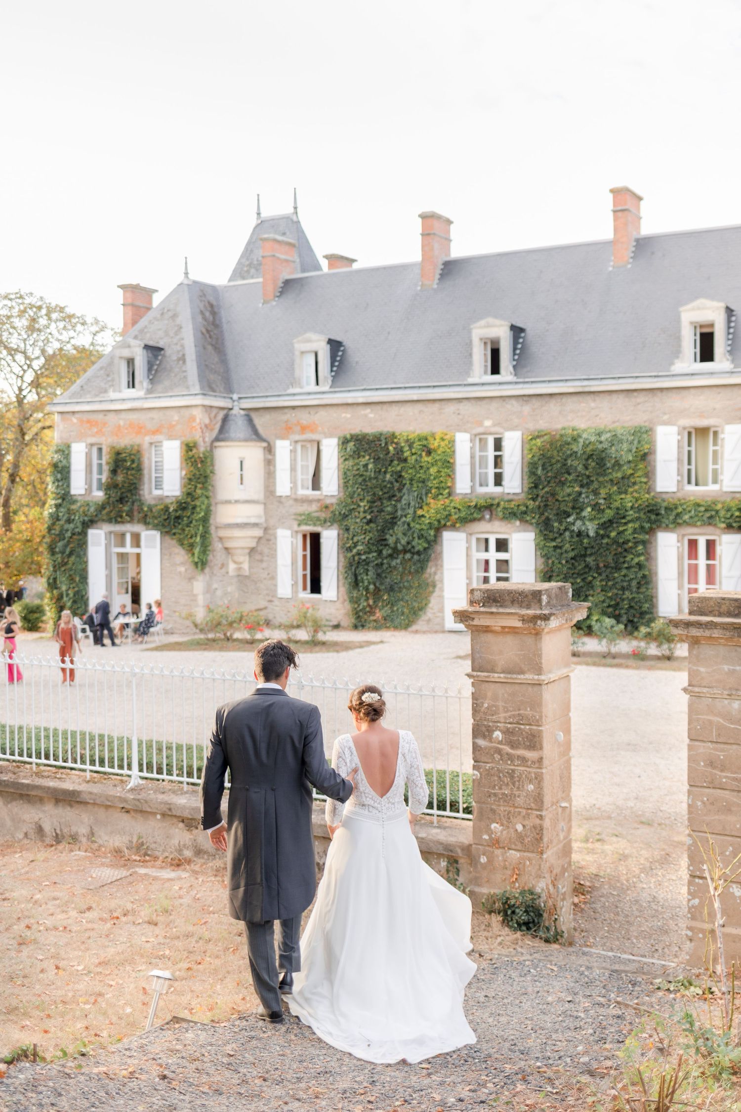Wedding couple walking away towards elegant French chateau with ivy-covered walls.