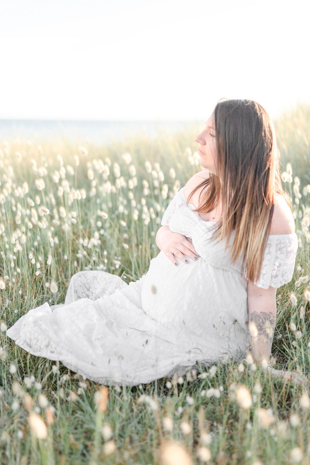 Side view of person in white lace dress sitting in coastal meadow.