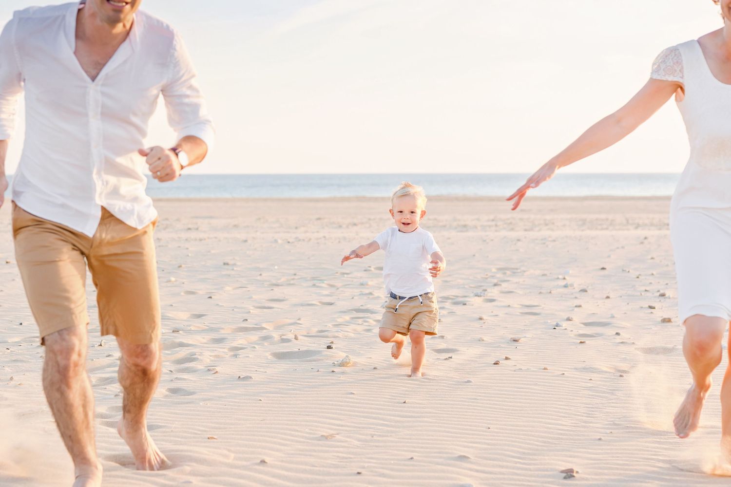 A small child jumping between two adults while playing on a sunny beach.