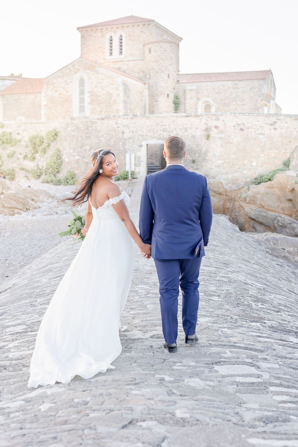 Wedding couple ascending stone steps together near historic building during sunset.
