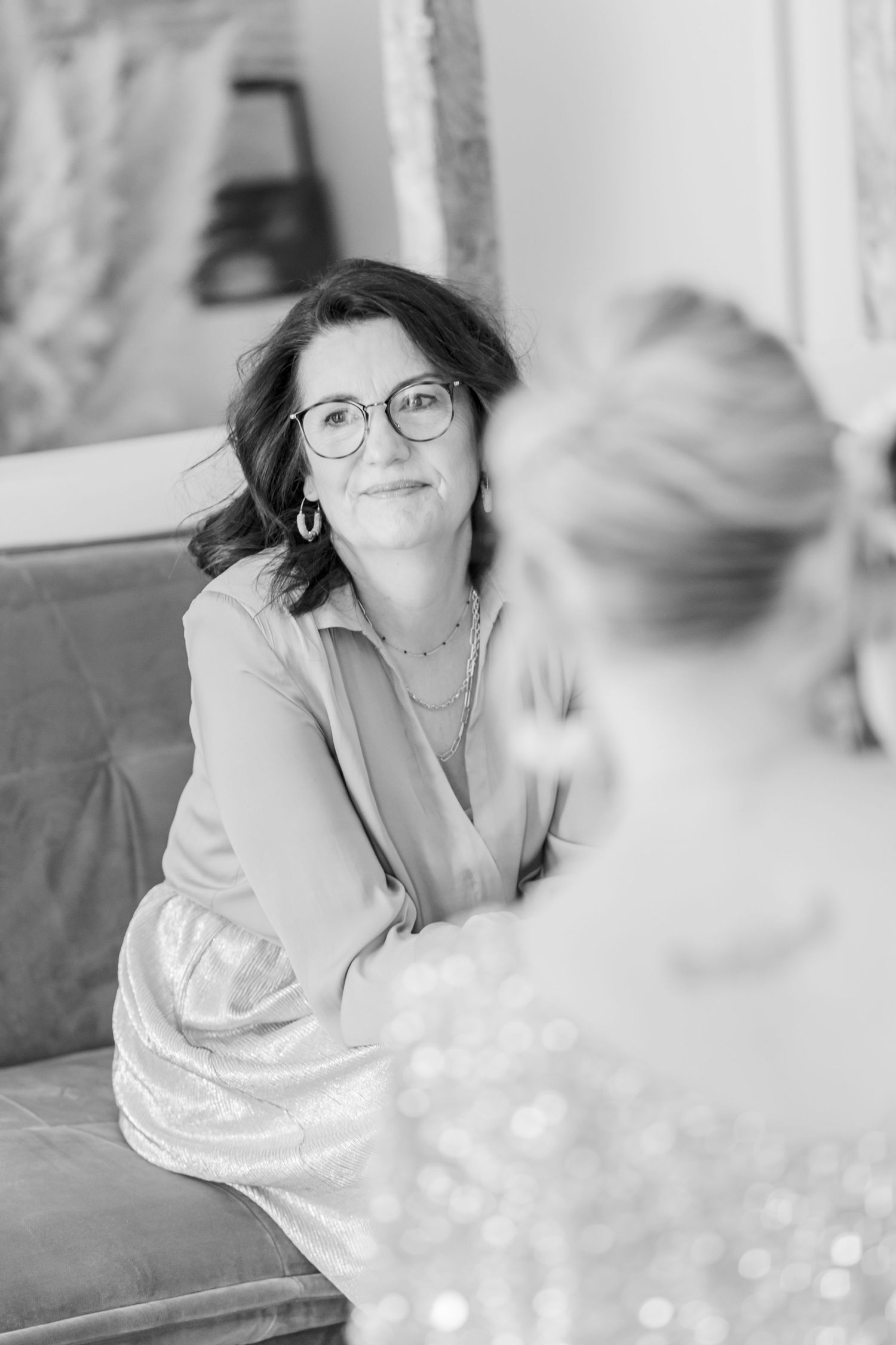 Two people having a conversation while seated on a gray couch in black and white photography.