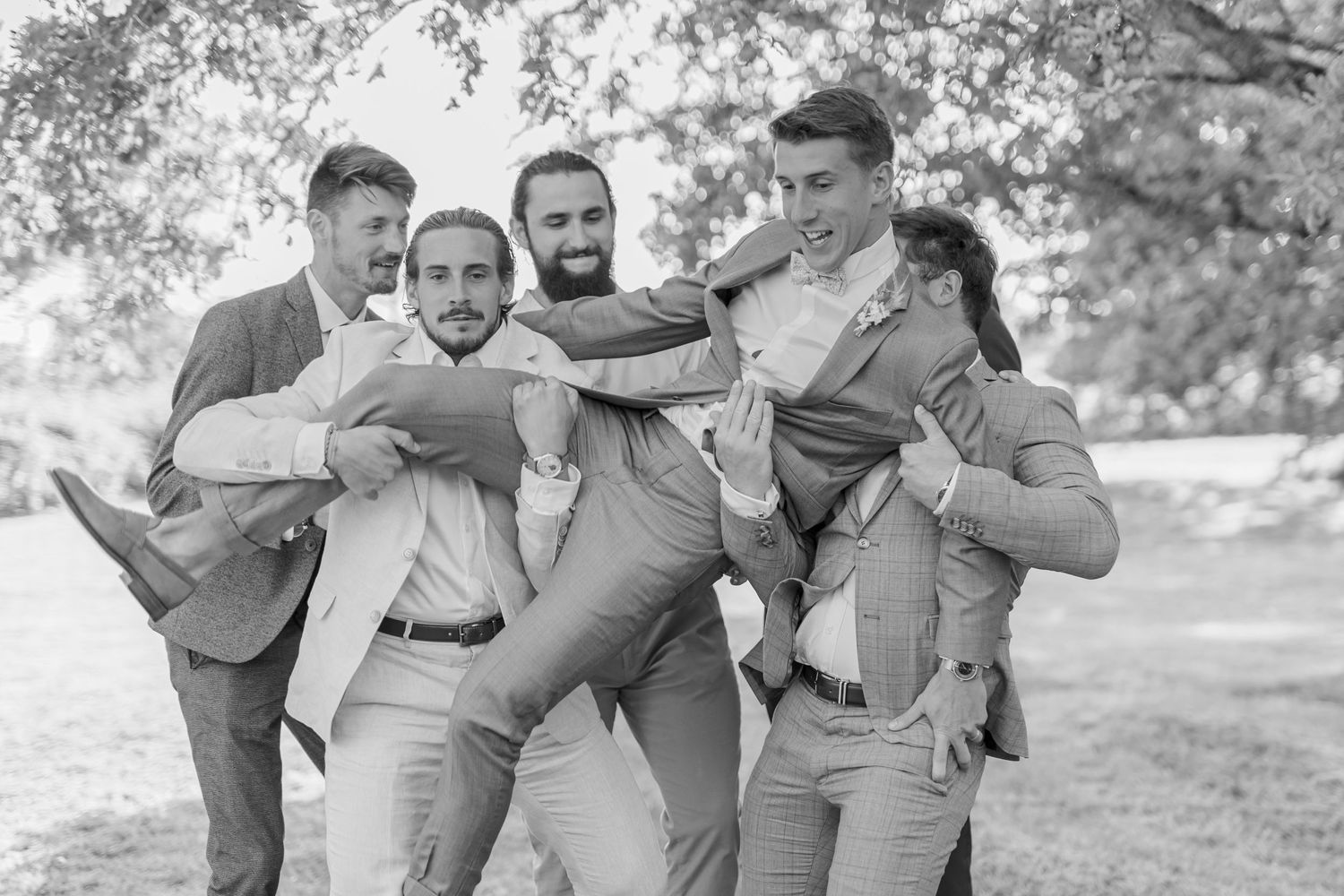 Groomsmen in gray suits share playful moments during outdoor wedding photography.