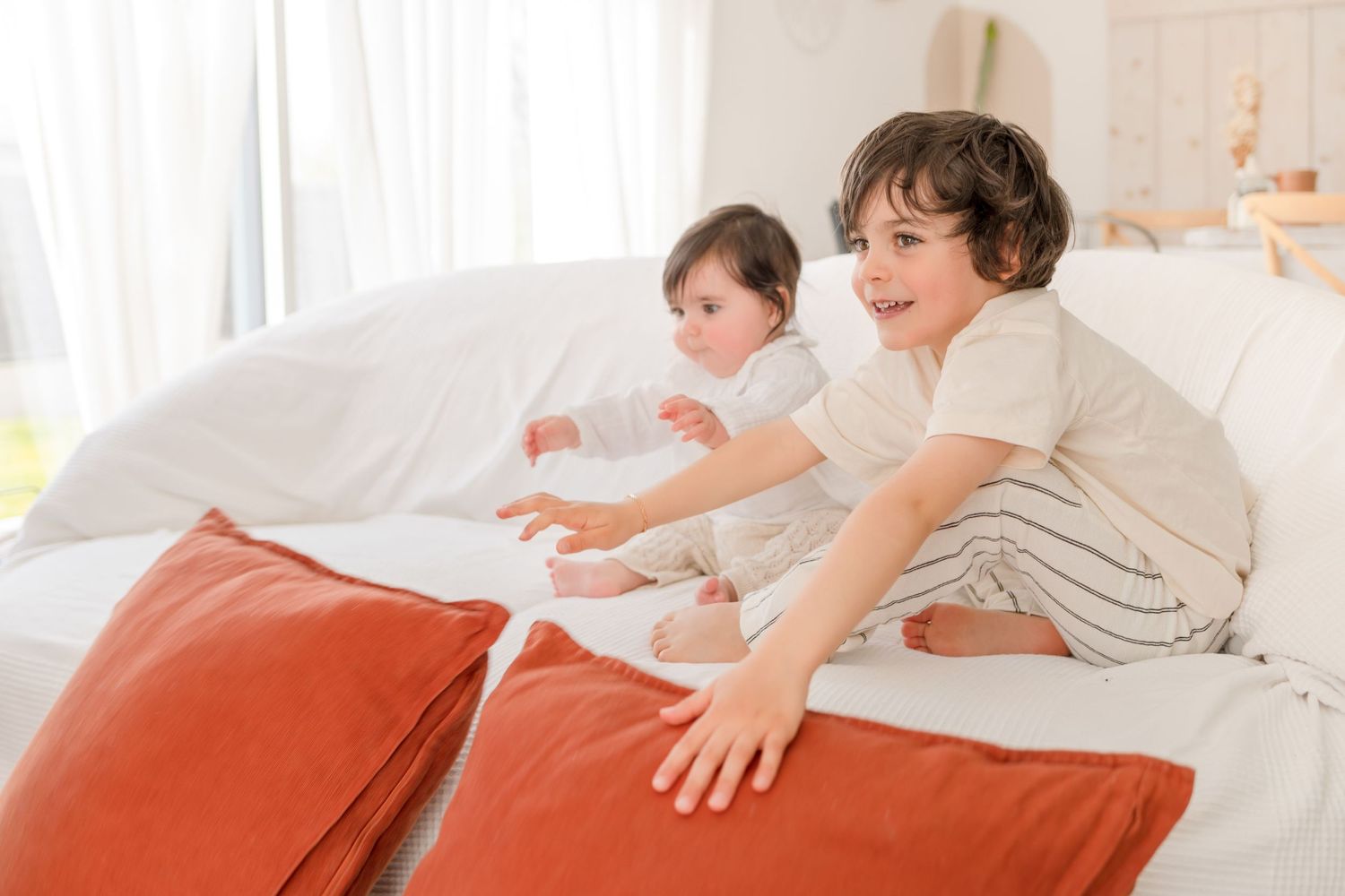 Children playing and jumping on a bed with bright orange pillows.