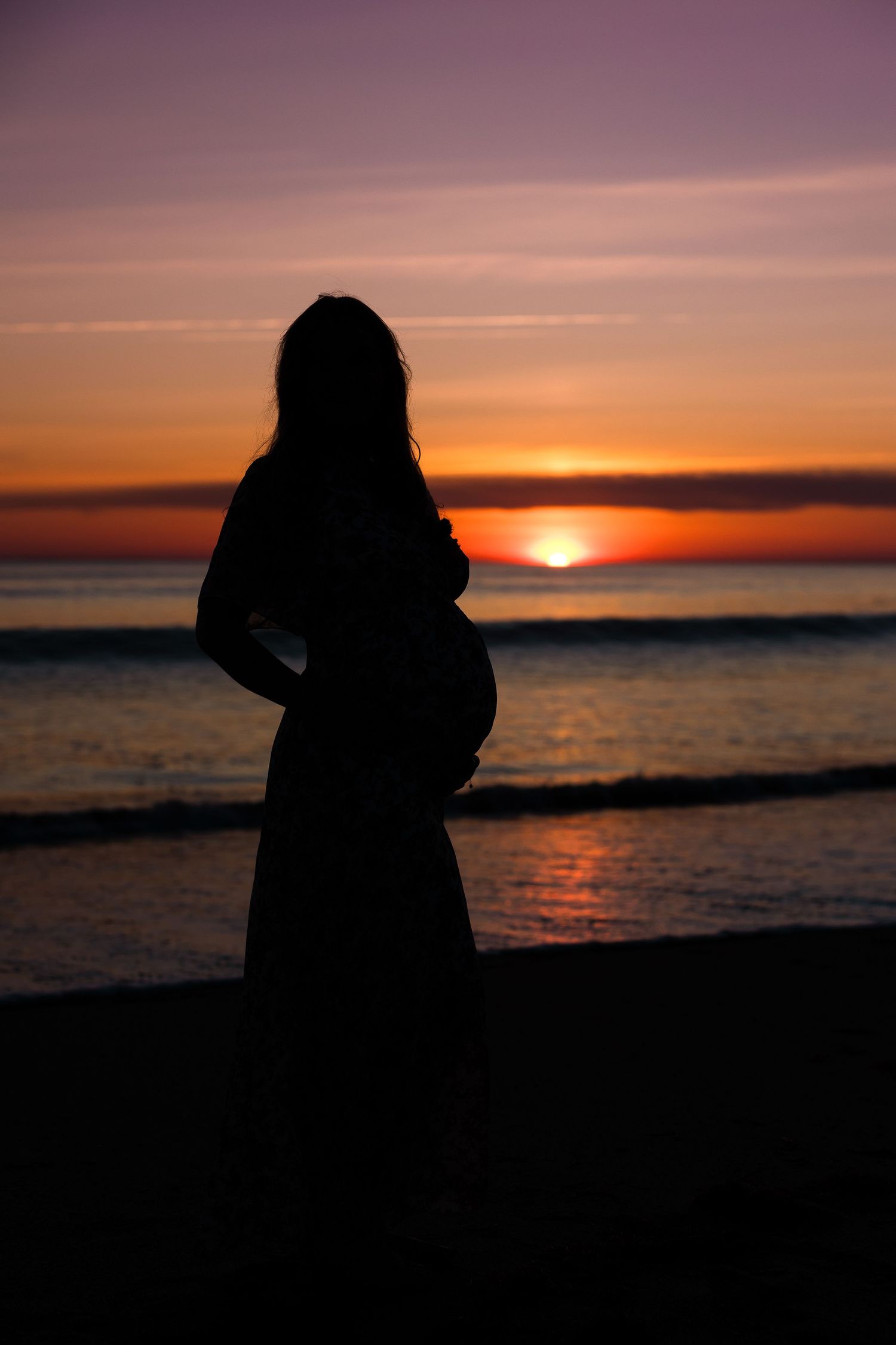 Dramatic silhouette portraits of couple against orange sunset over ocean.