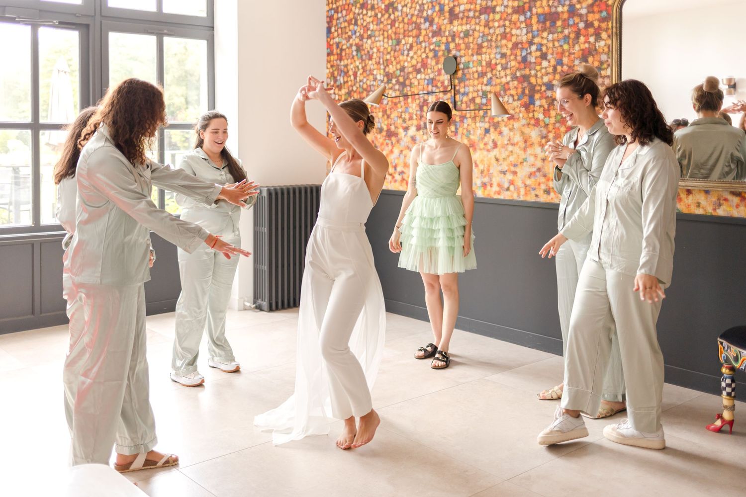 Wedding celebration with guests dancing in light colored attire against an orange accent wall.