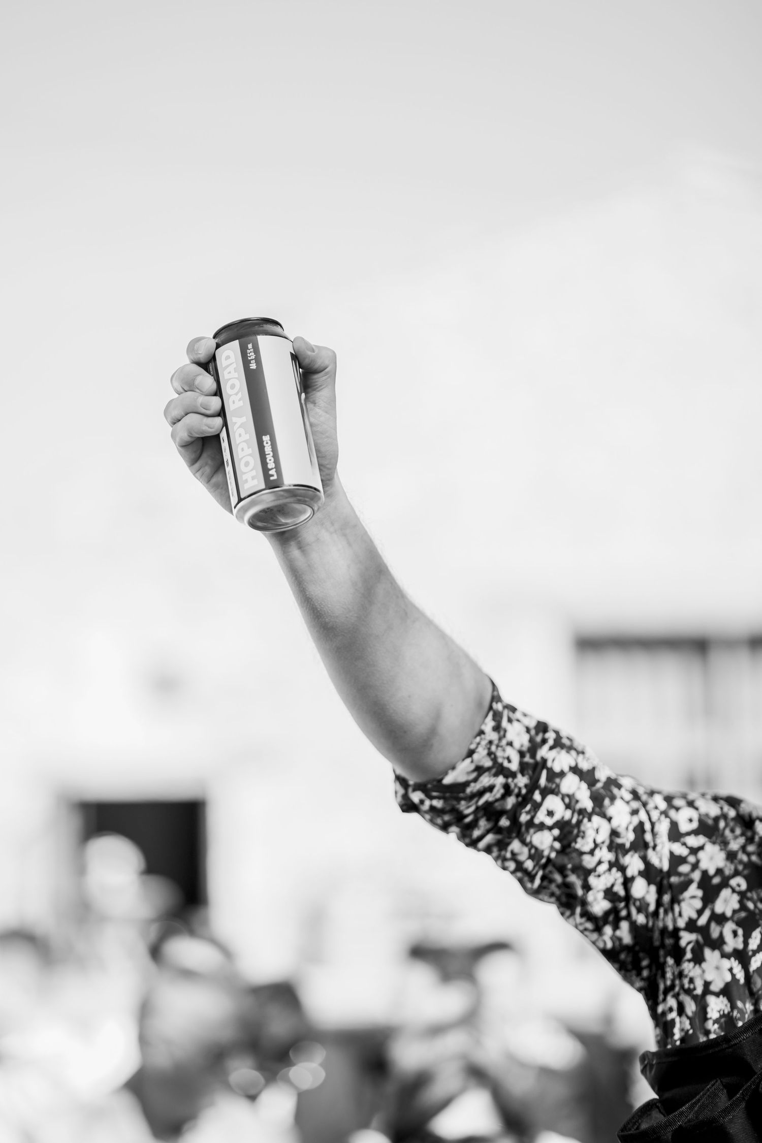 Black and white photo of raised arm holding a drink can against bright sky.