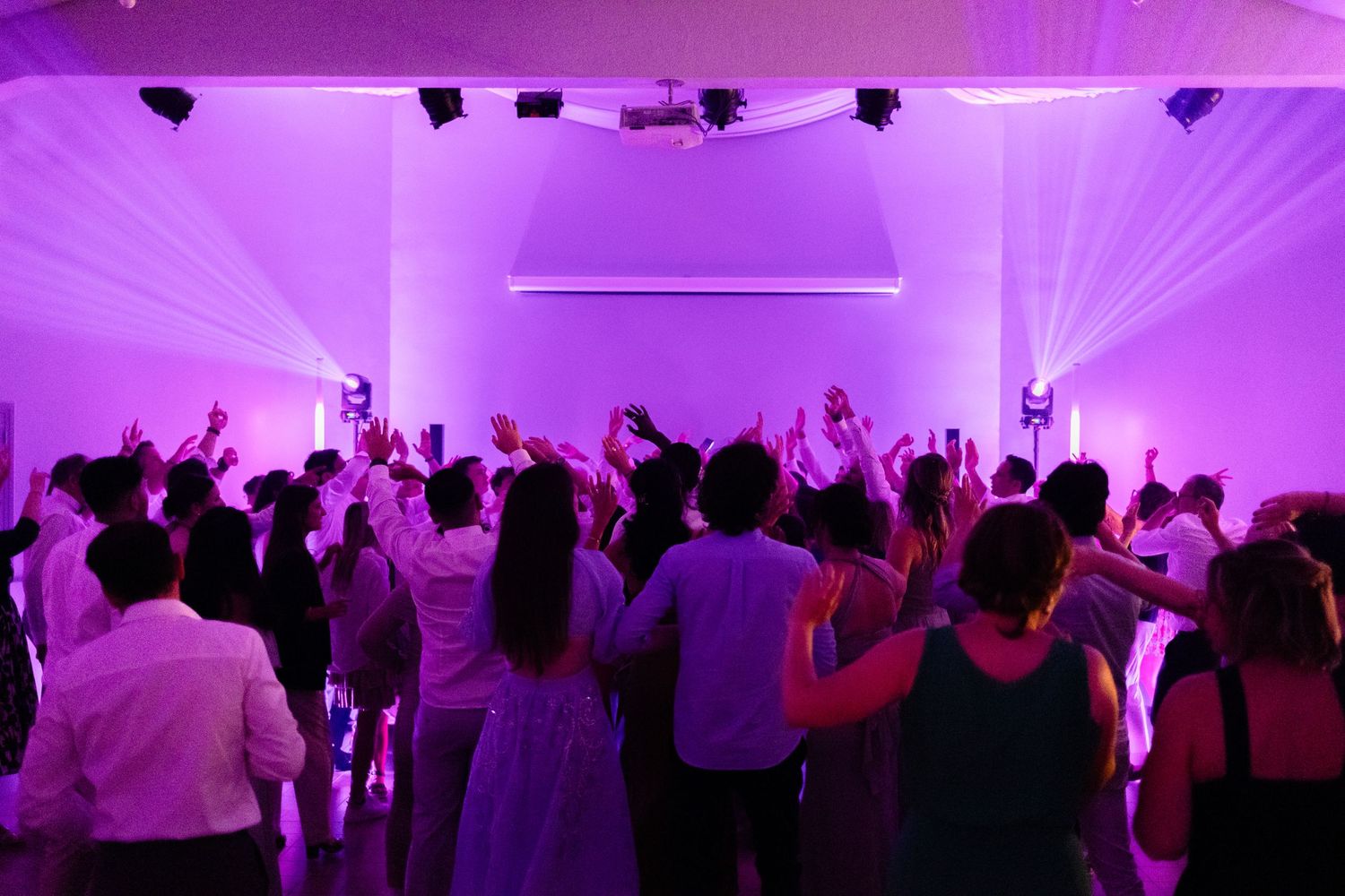 Dance floor filled with party guests under purple lighting and laser effects.
