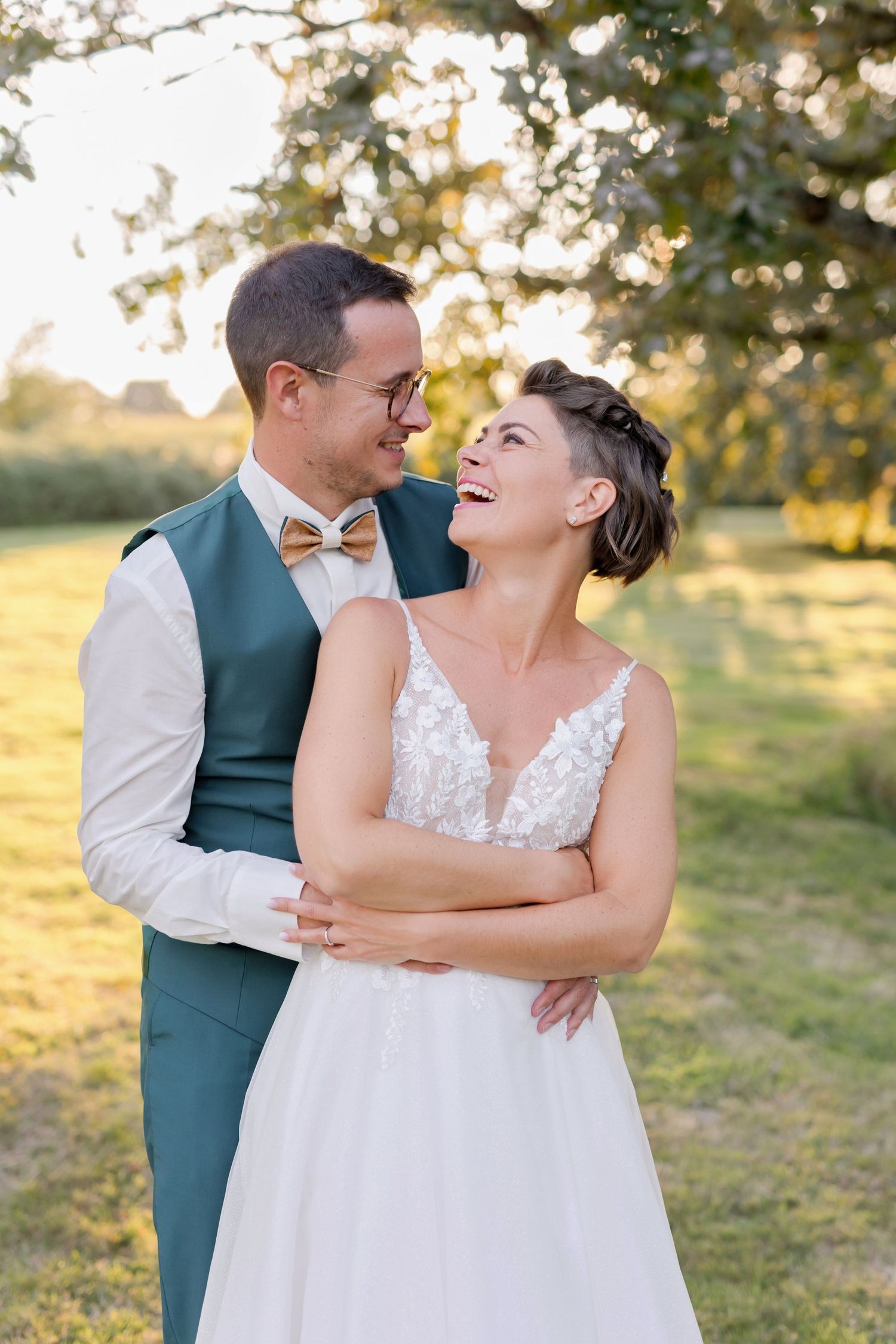 Happy couple in wedding attire laughing together in sunlit garden.