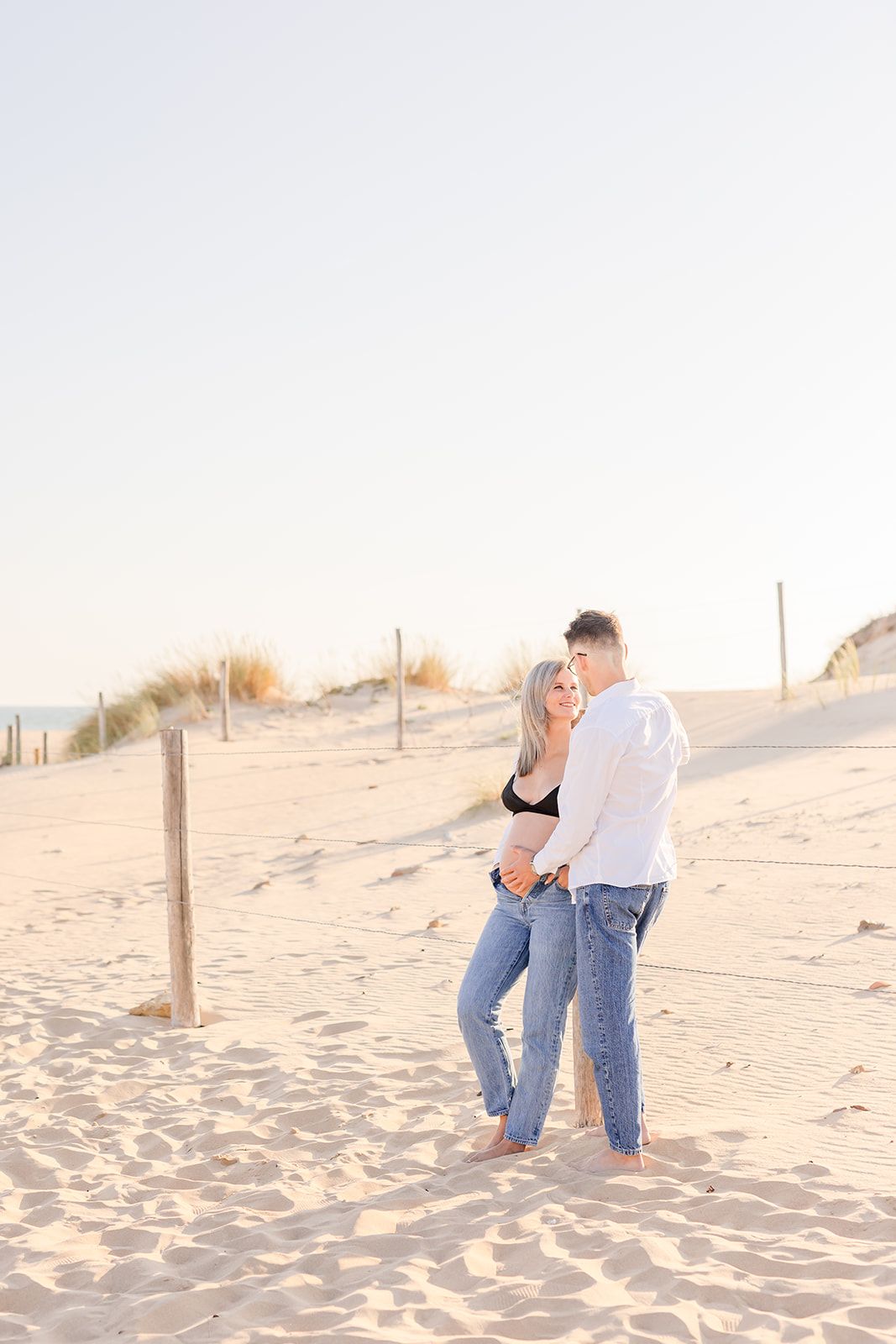 Couple embracing on a sandy beach during golden hour with sand dunes in the background.