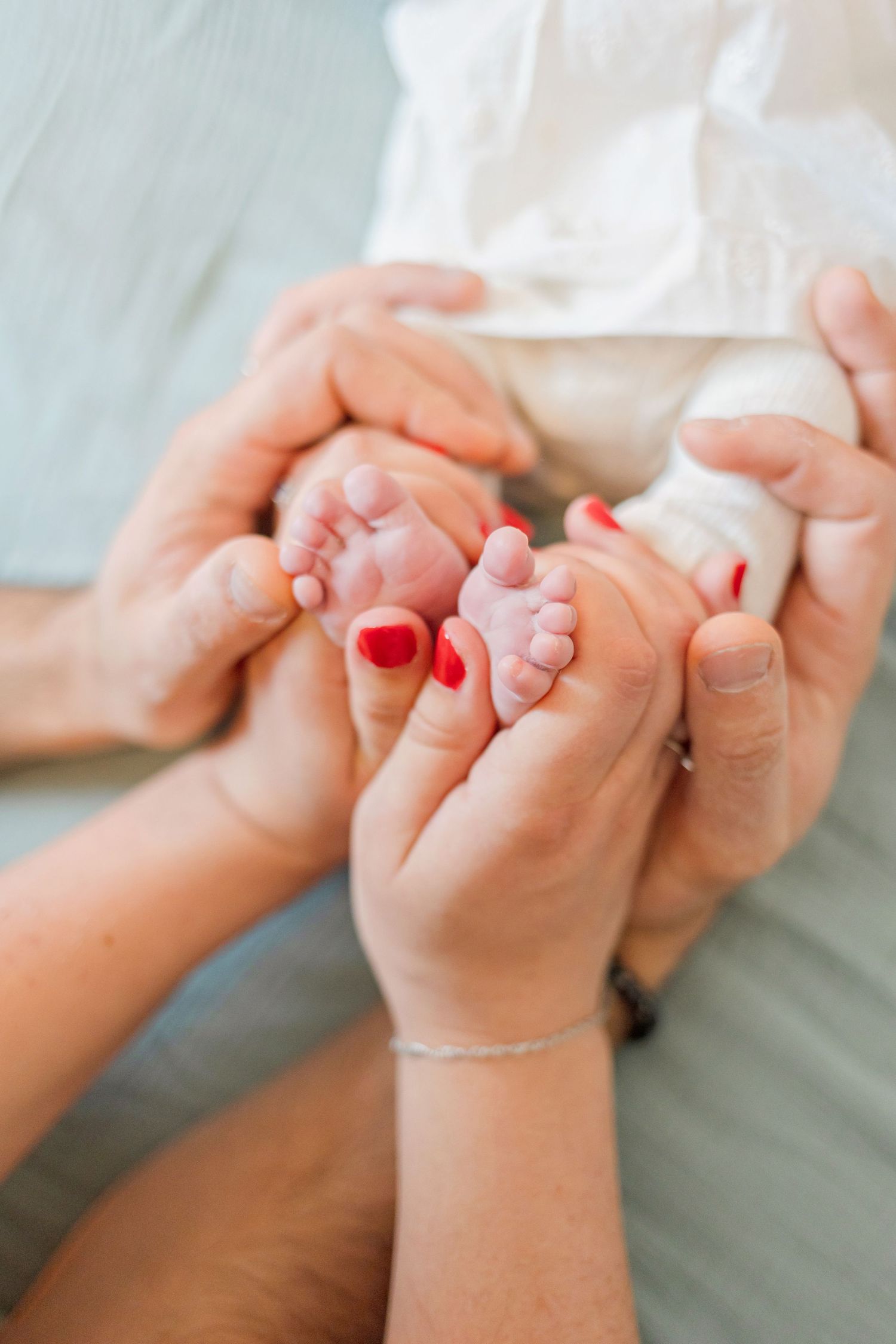 Close-up of tiny baby feet being tenderly held by hands with red nail polish.