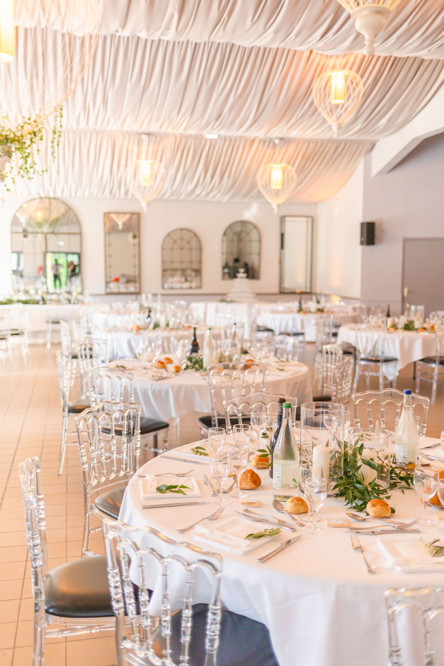 Elegant wedding reception venue with draped ceiling, crystal chandeliers and white table settings.