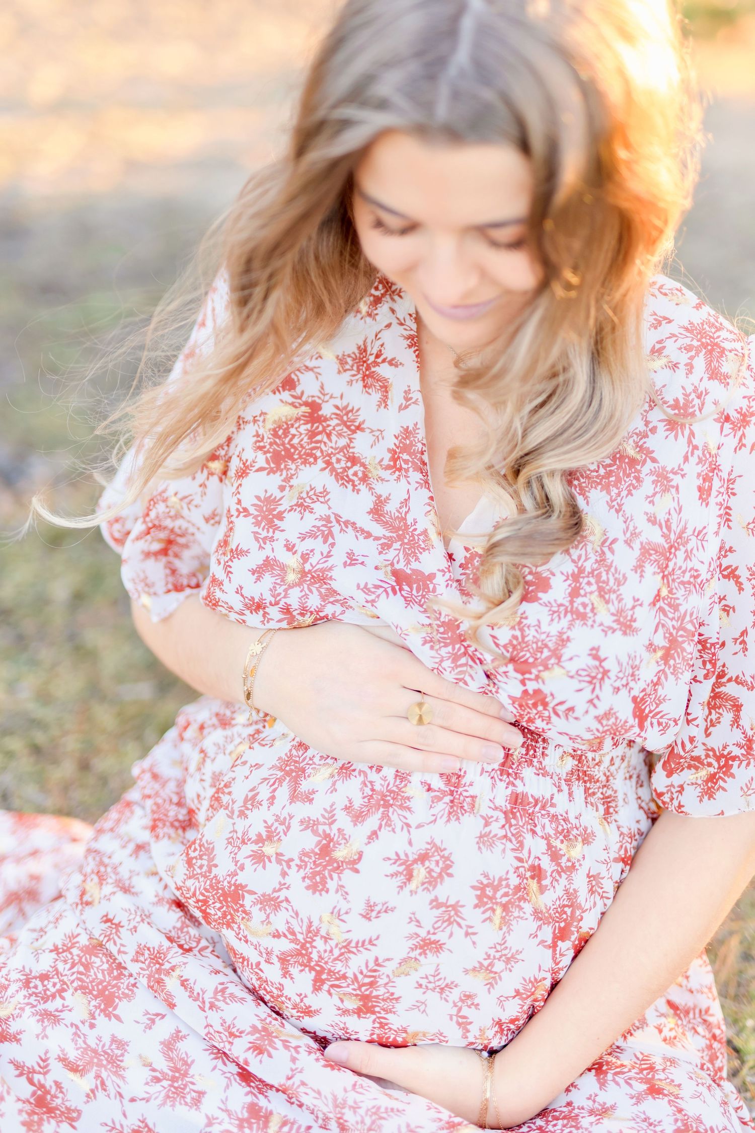 Woman in red floral dress cradling her baby bump during maternity photoshoot.