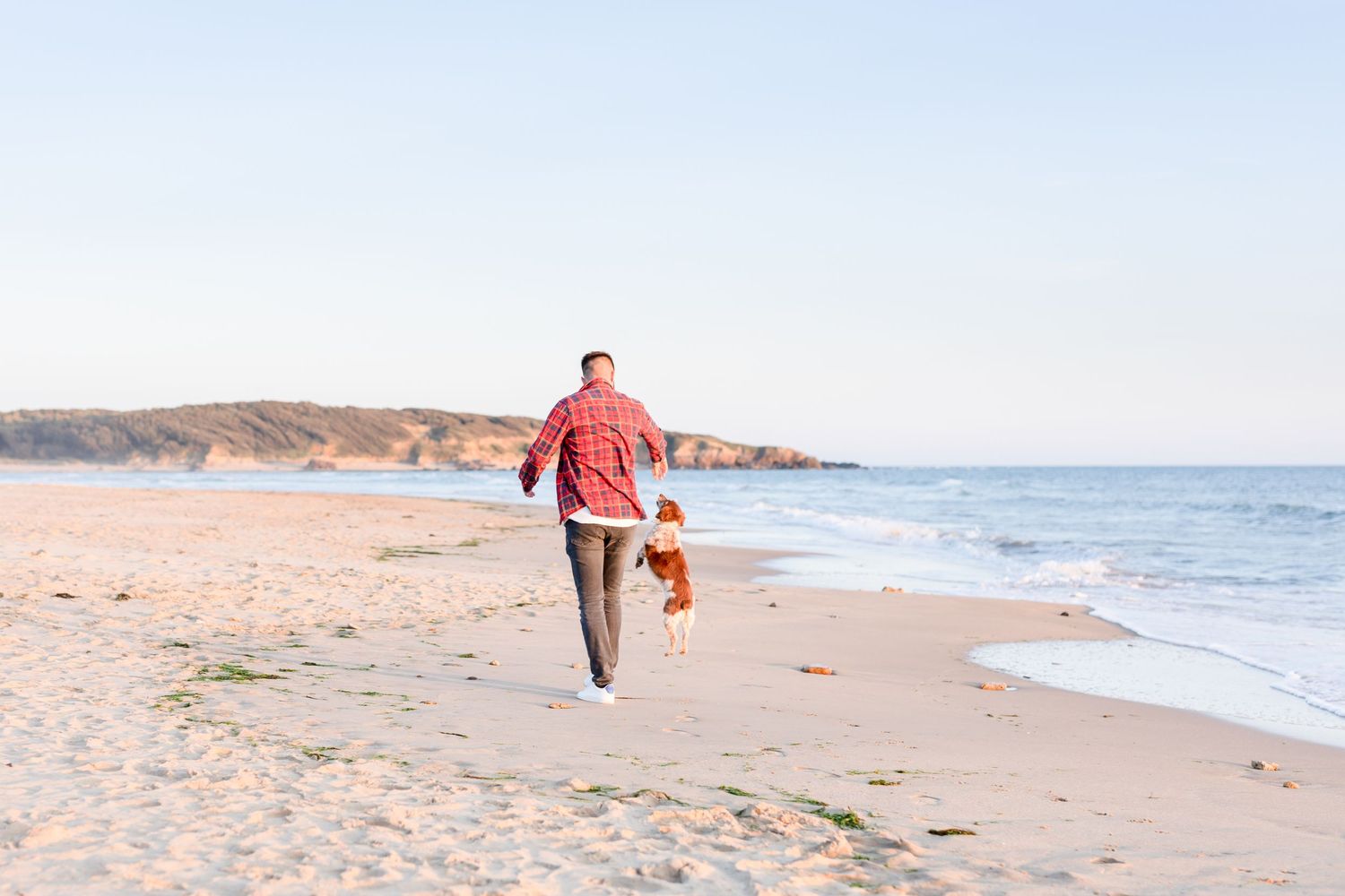 Person in red shirt running joyfully along the shoreline at sunset.