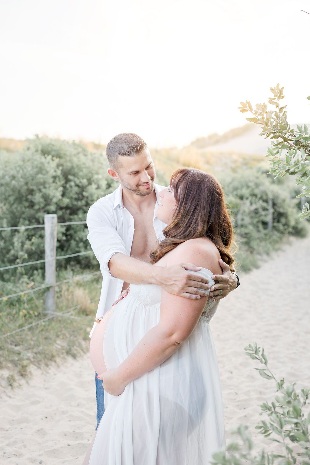 A joyful maternity portrait capturing a loving embrace on a hillside trail during golden hour.