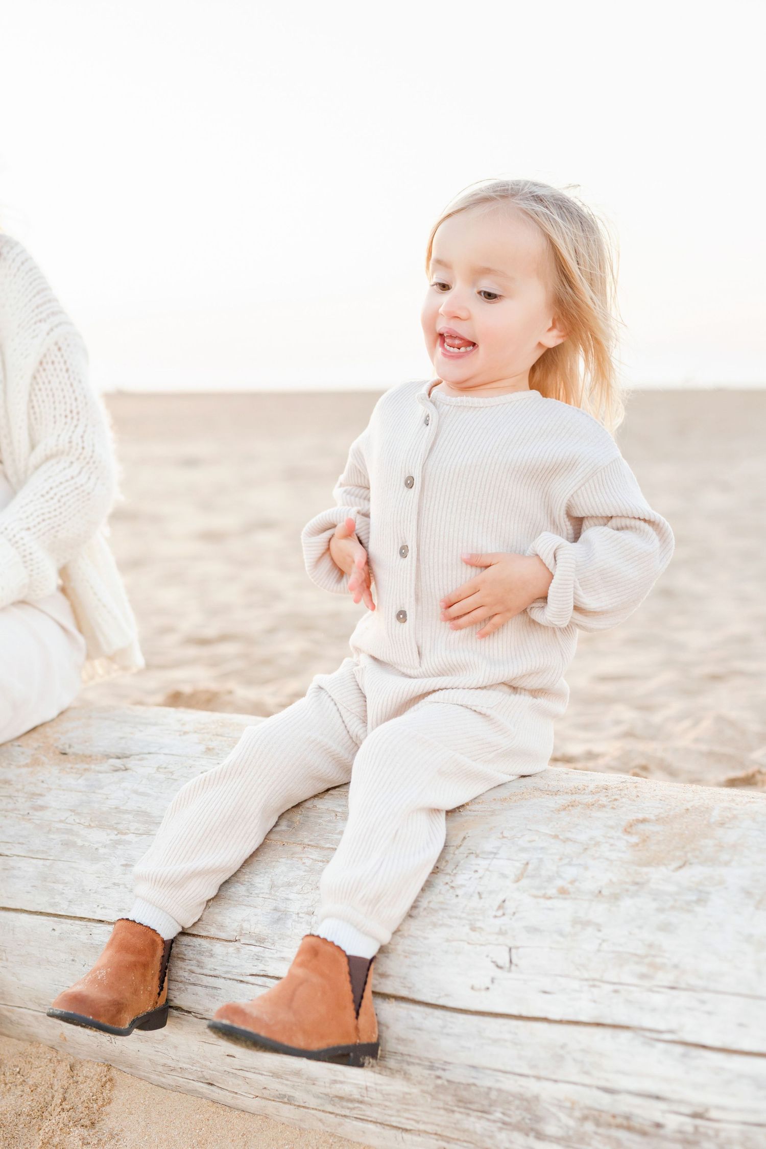 Toddler in cream-colored outfit sitting on wooden planks at the beach.