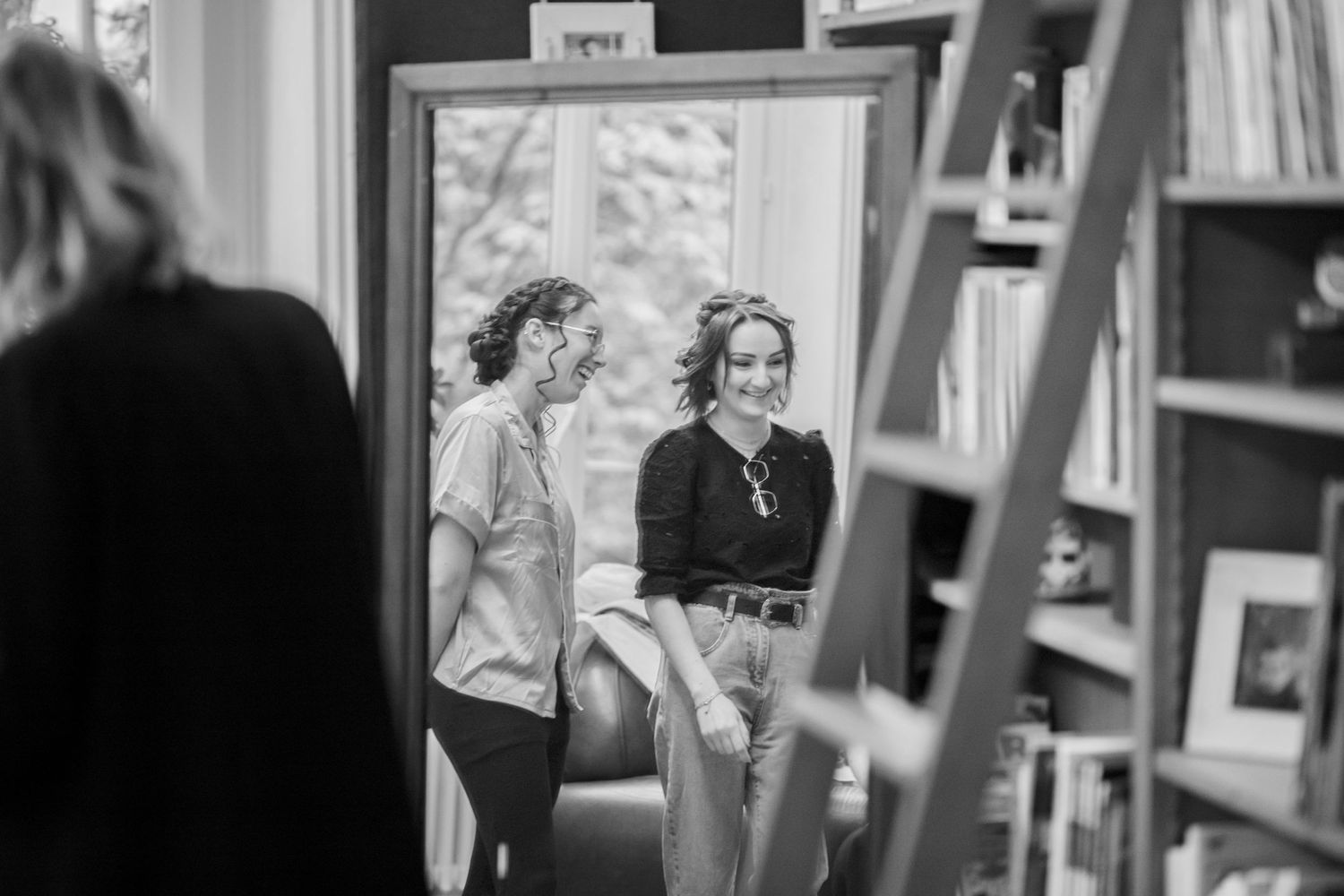 Black and white photograph of two people talking in a room with bookshelves.