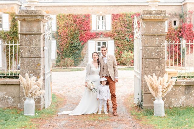 Elegant wedding party gathered outside a stone mansion with climbing red vines.