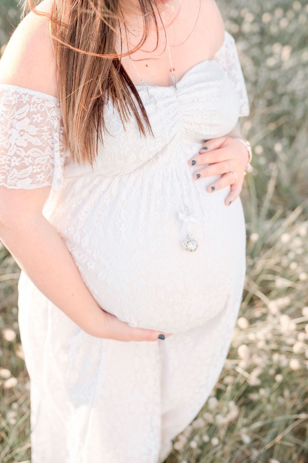 Close-up maternity photo showcasing white lace dress details and baby bump.
