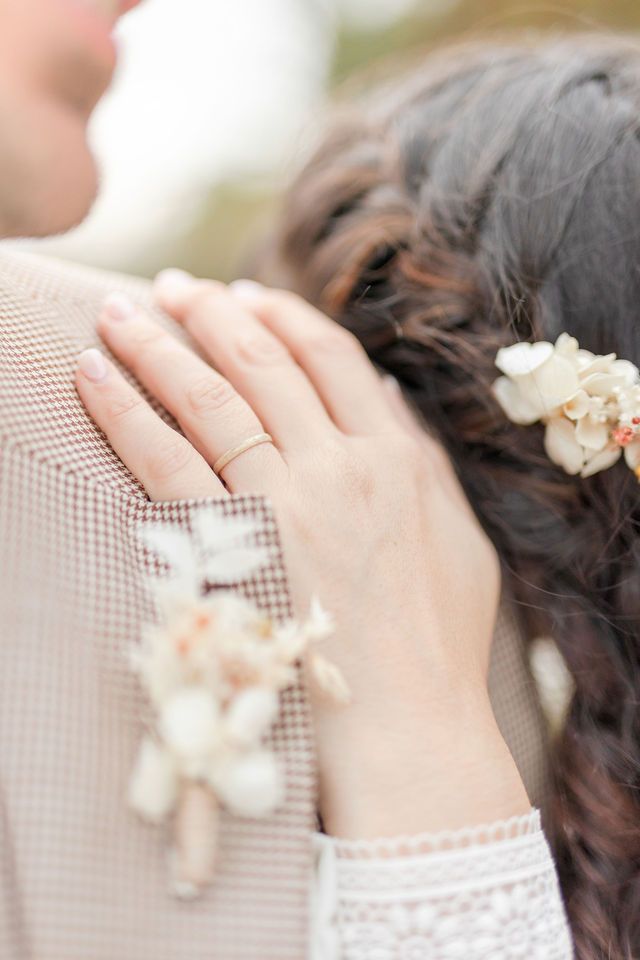 Close up of hands touching with small white flowers in hair against beige suit.