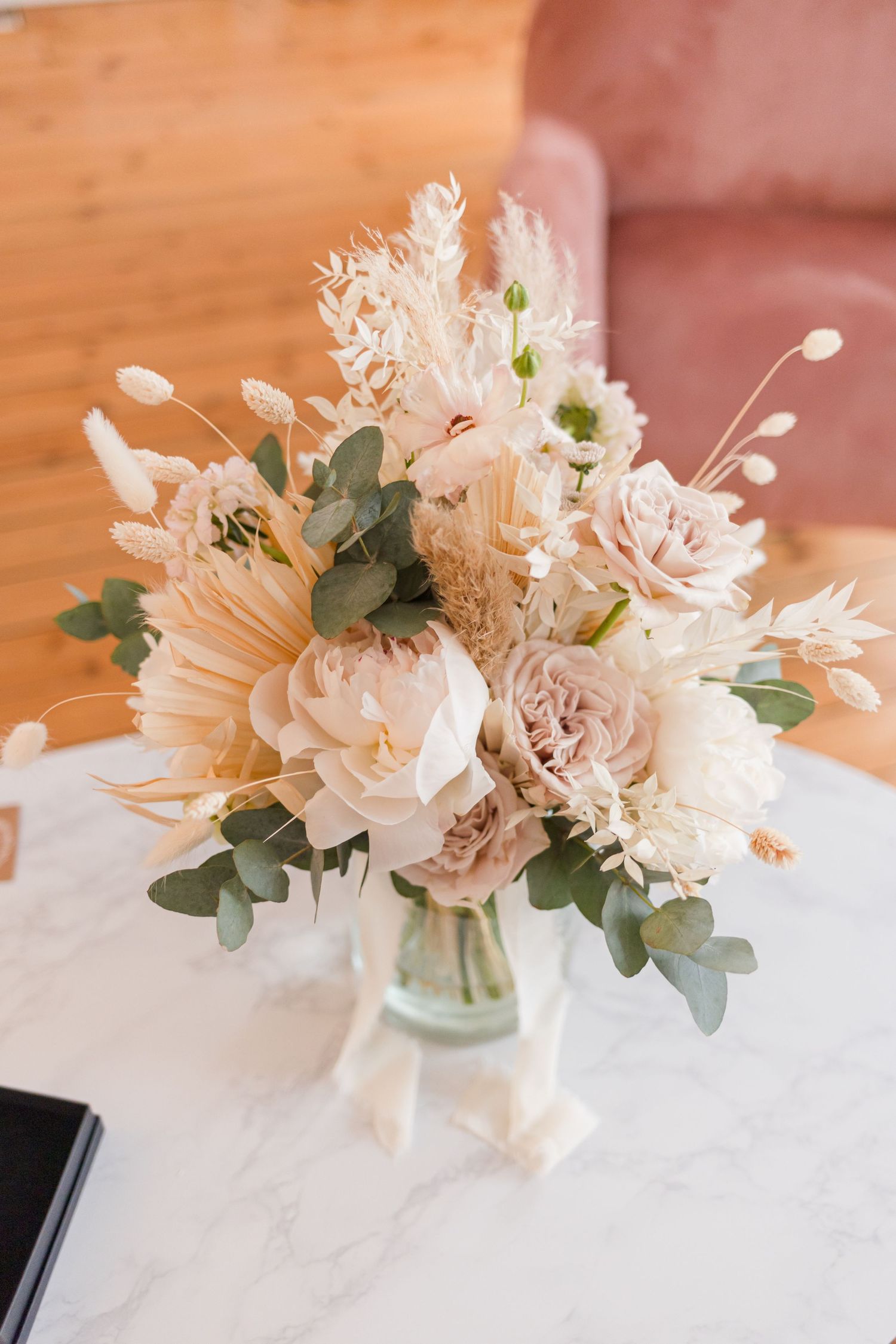 Elegant floral arrangement with white and blush roses, eucalyptus in glass vase on marble table.