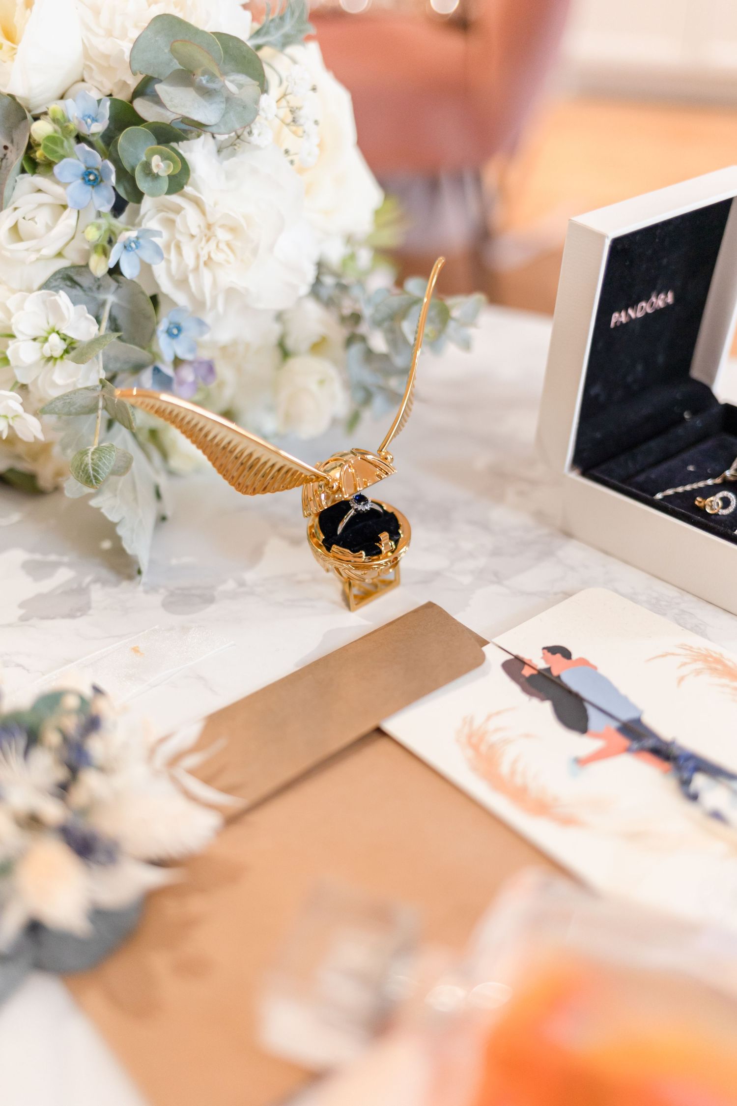 Wedding details with golden snitch, floral arrangements and photo cards on table.