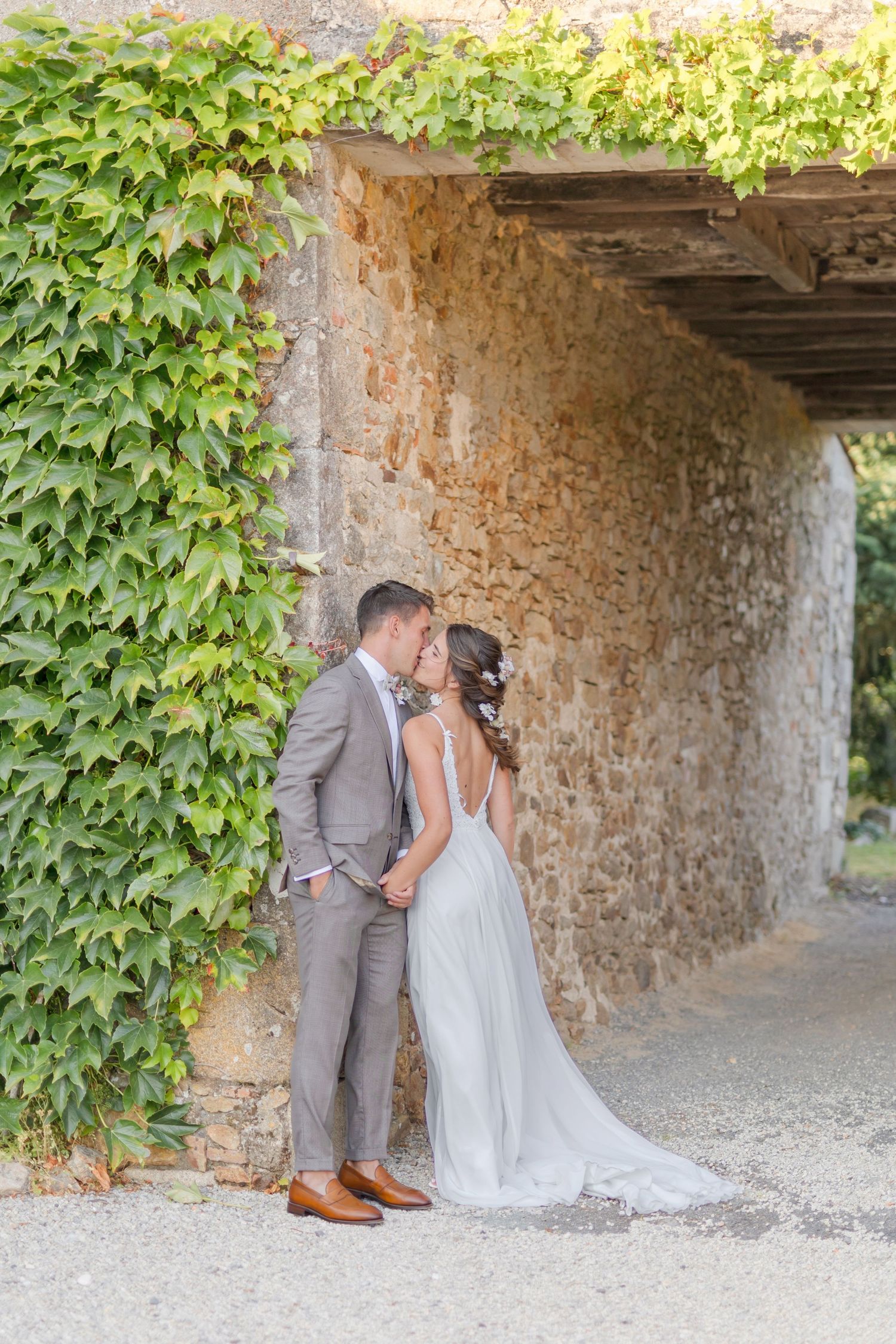 Intimate wedding moment captured against rustic stone archway with climbing vines.