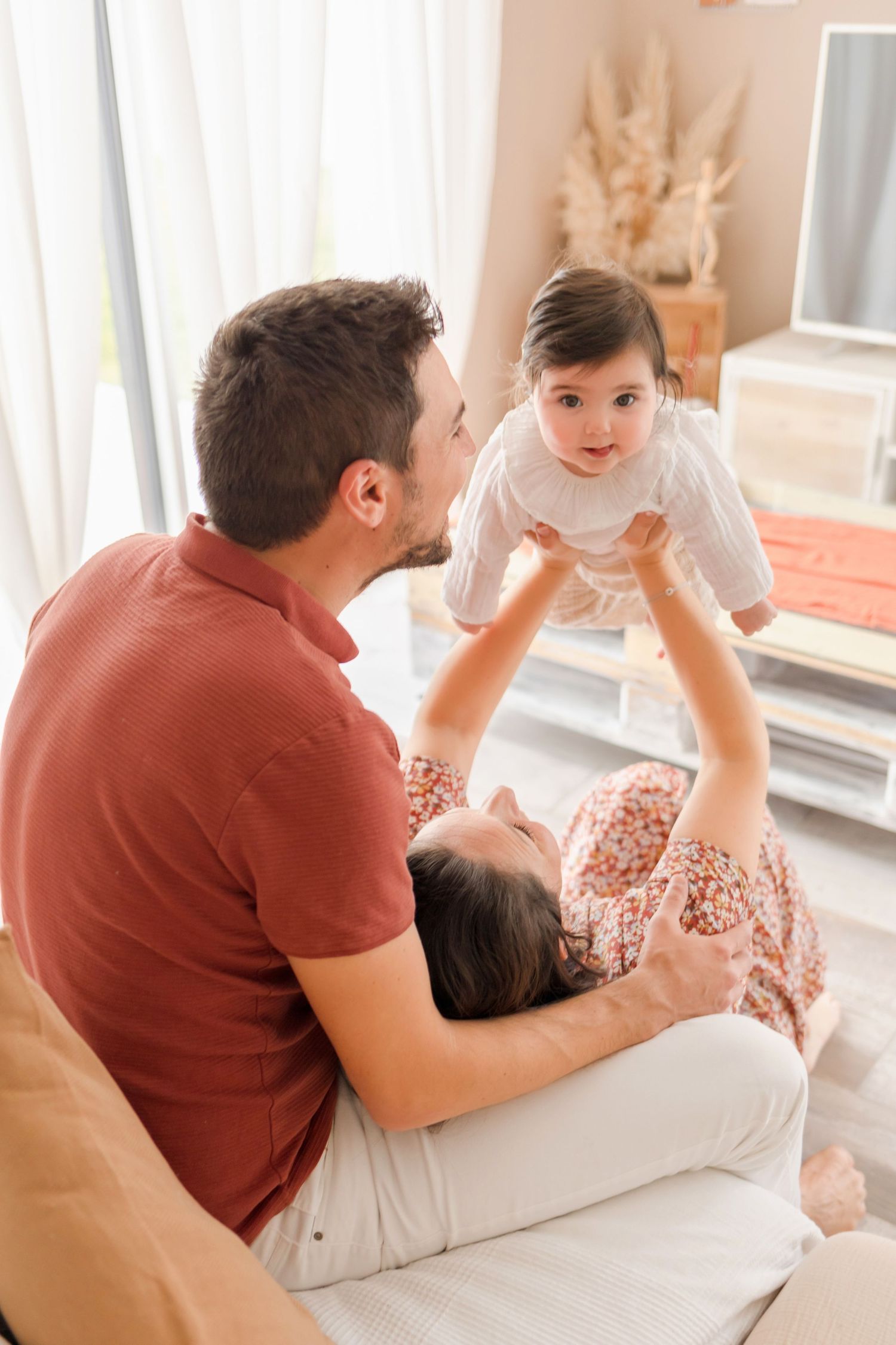 A playful family moment captured on white bedding in a bright, airy room.