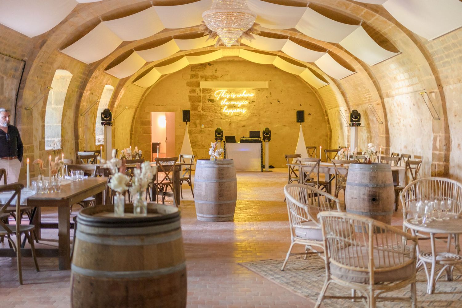 Rustic event venue with barrel decor and rattan chairs under vaulted stone ceiling.